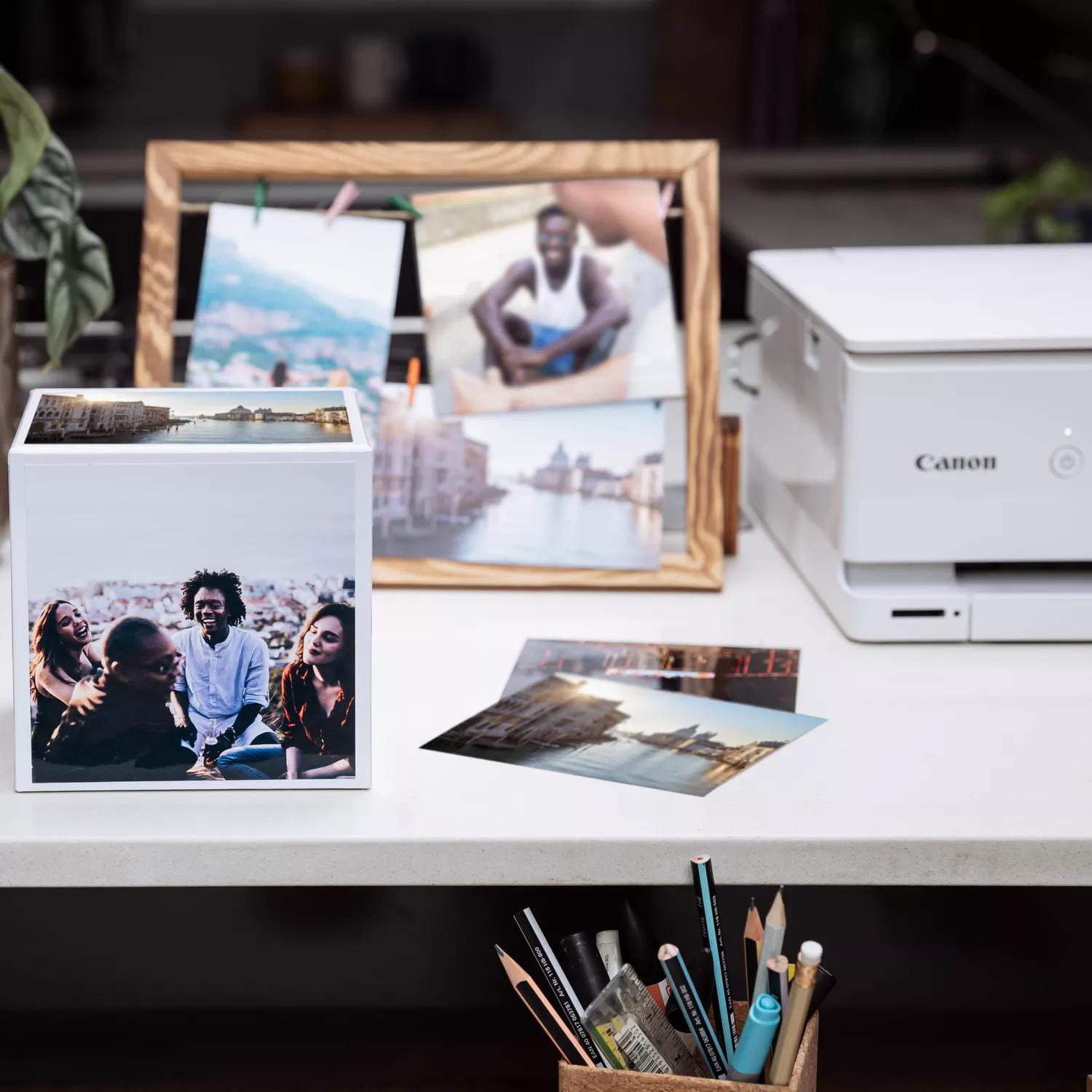 Fotos und Drucker auf einem Tisch. Fotos in einem Rahmen und einer weißen Box. Canon-Drucker im Hintergrund.