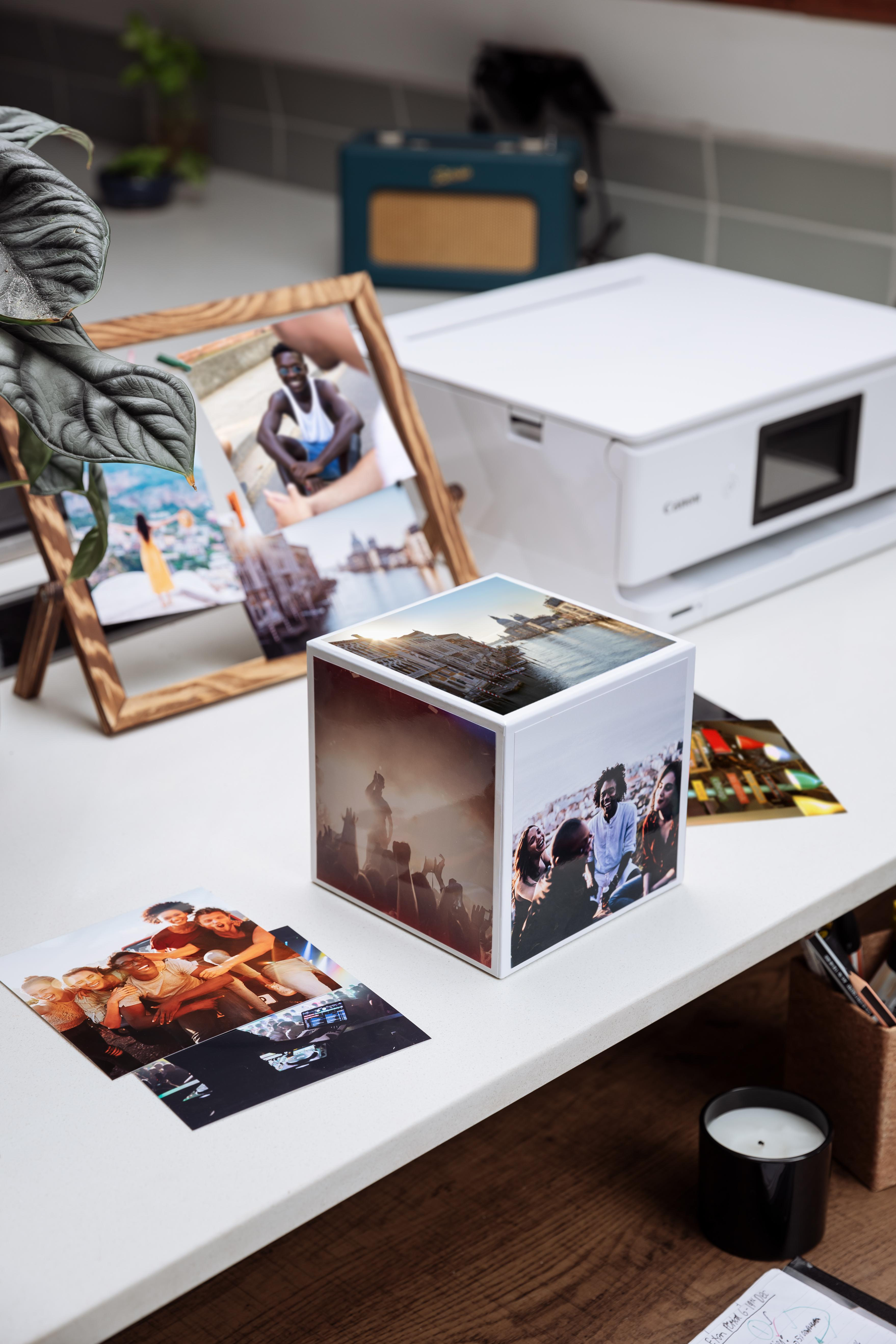 Fotos auf einem Schreibtisch, mit Drucker, Kerze und Fotowürfel.