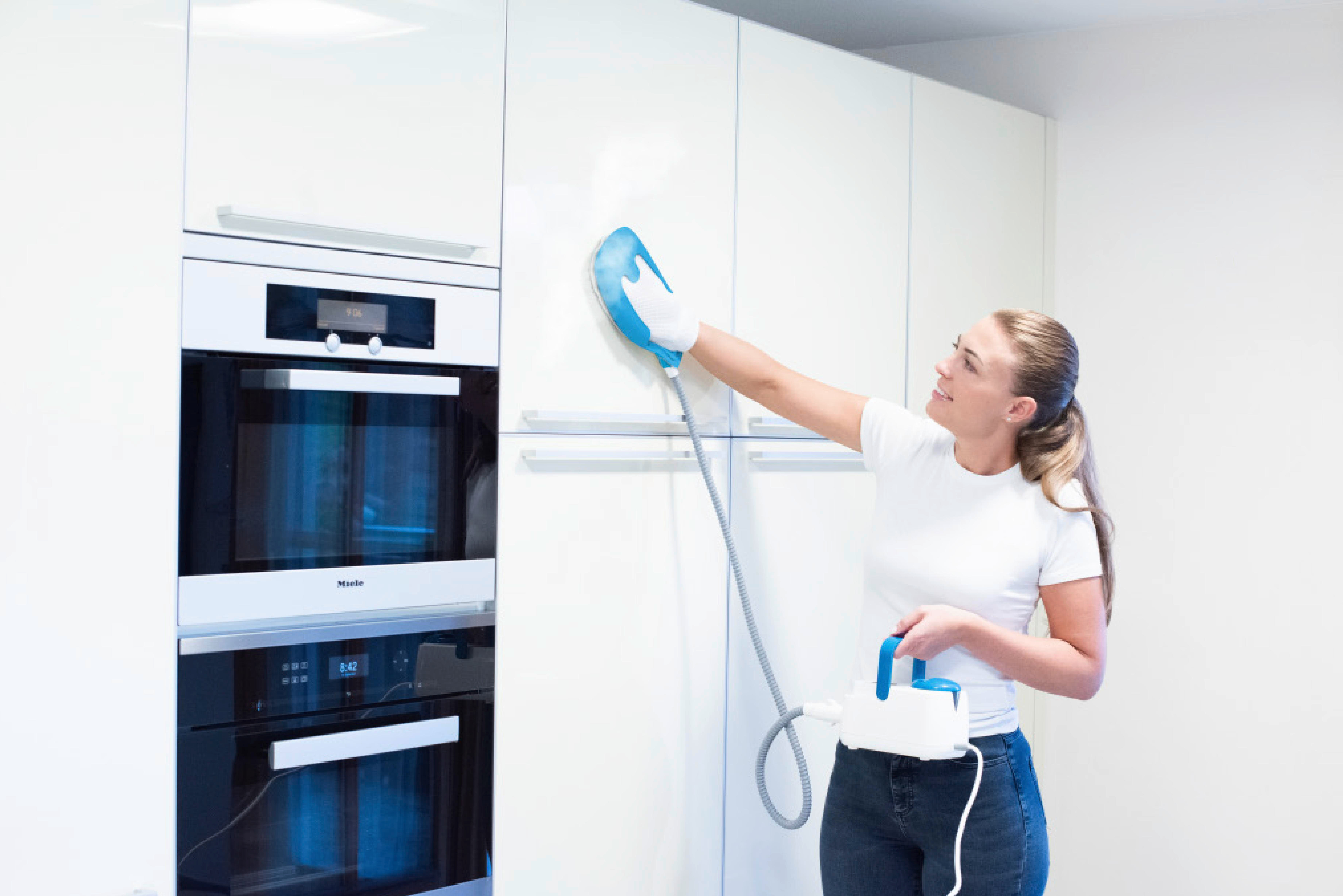 Eine Frau reinigt einen weißen Schrank mit einem Dampfreiniger.