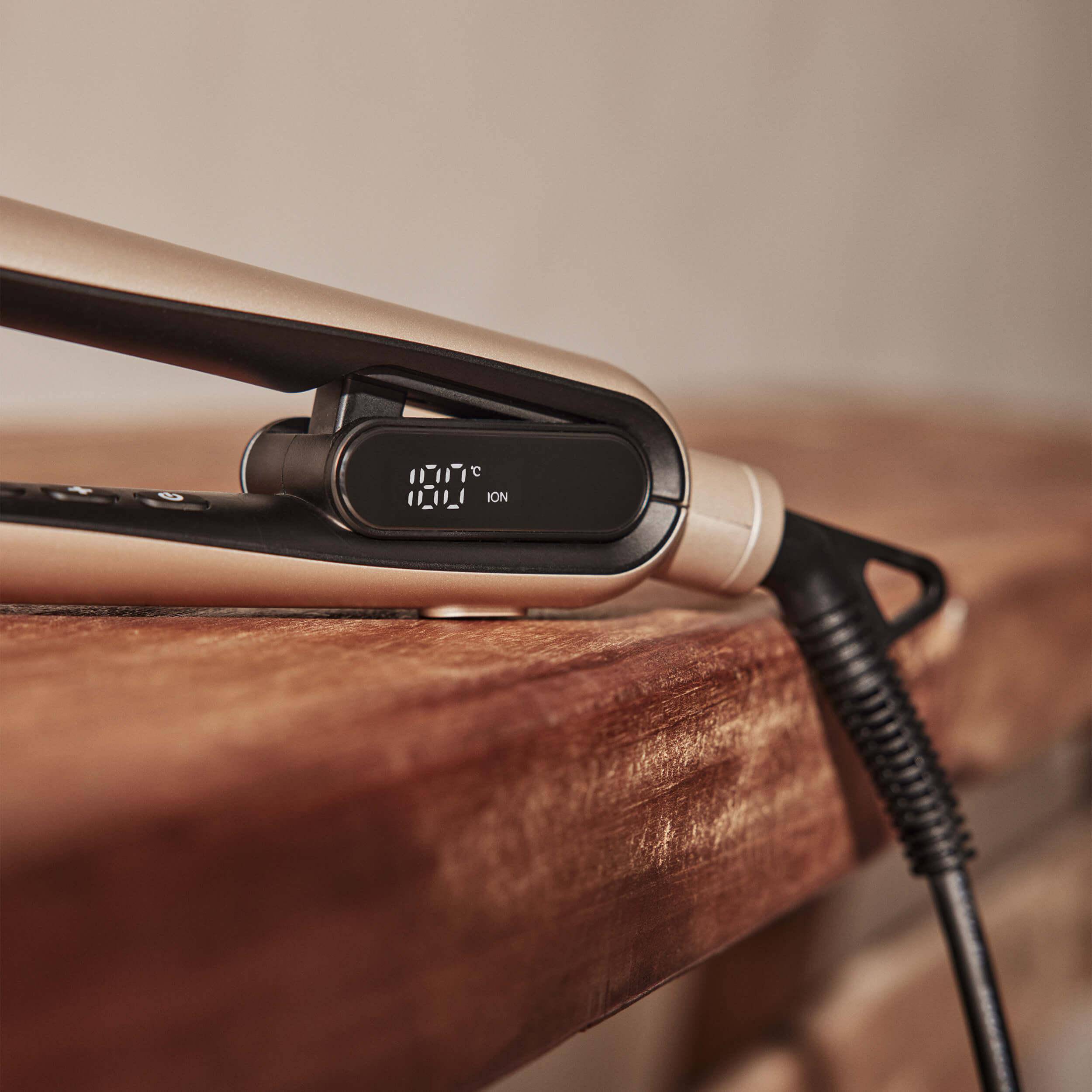 Haarglätter mit Digitalanzeige der Temperatur, auf Holzoberfläche platziert.