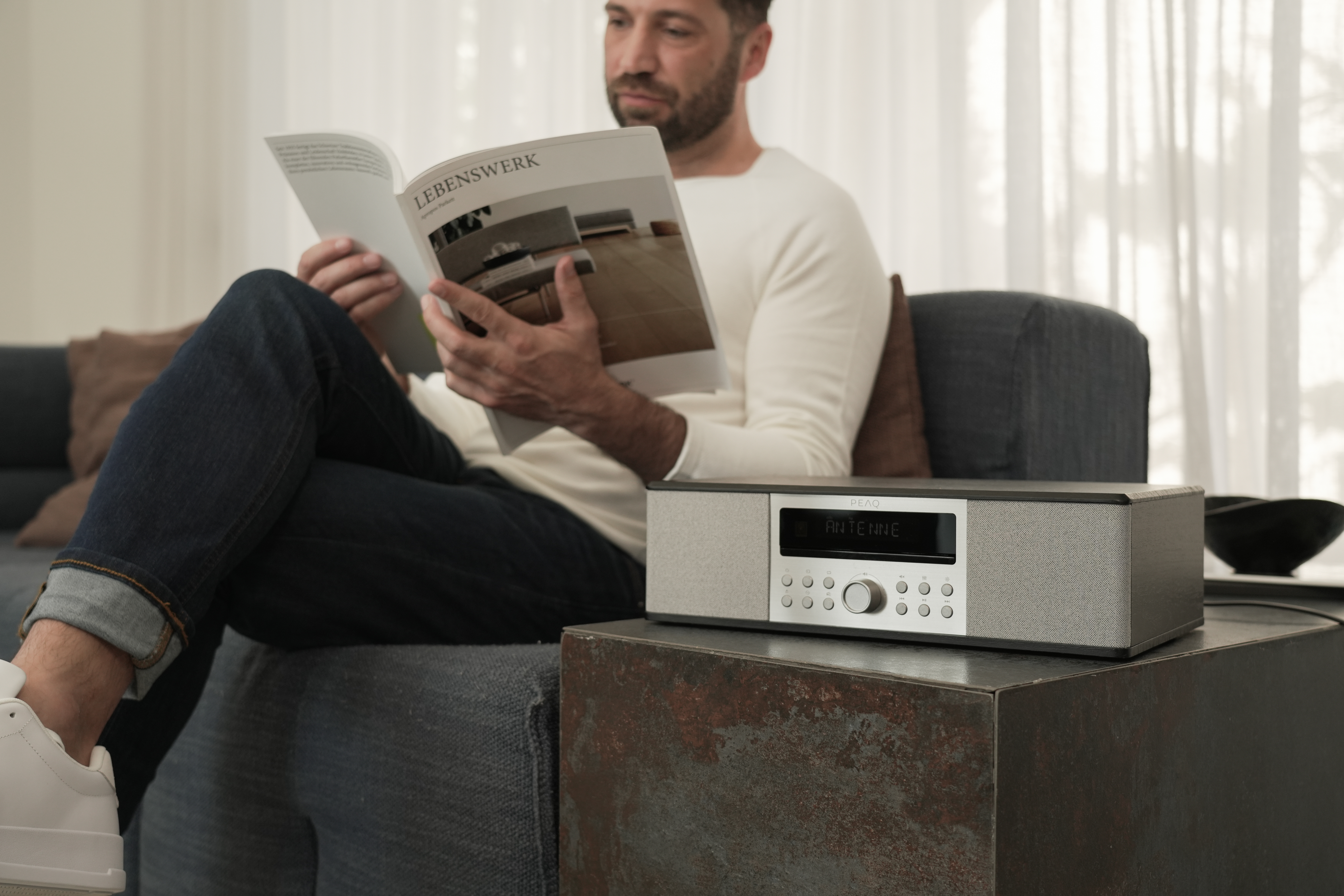 Ein Mann liest ein Buch, während er auf einer Couch neben einem Radio sitzt.