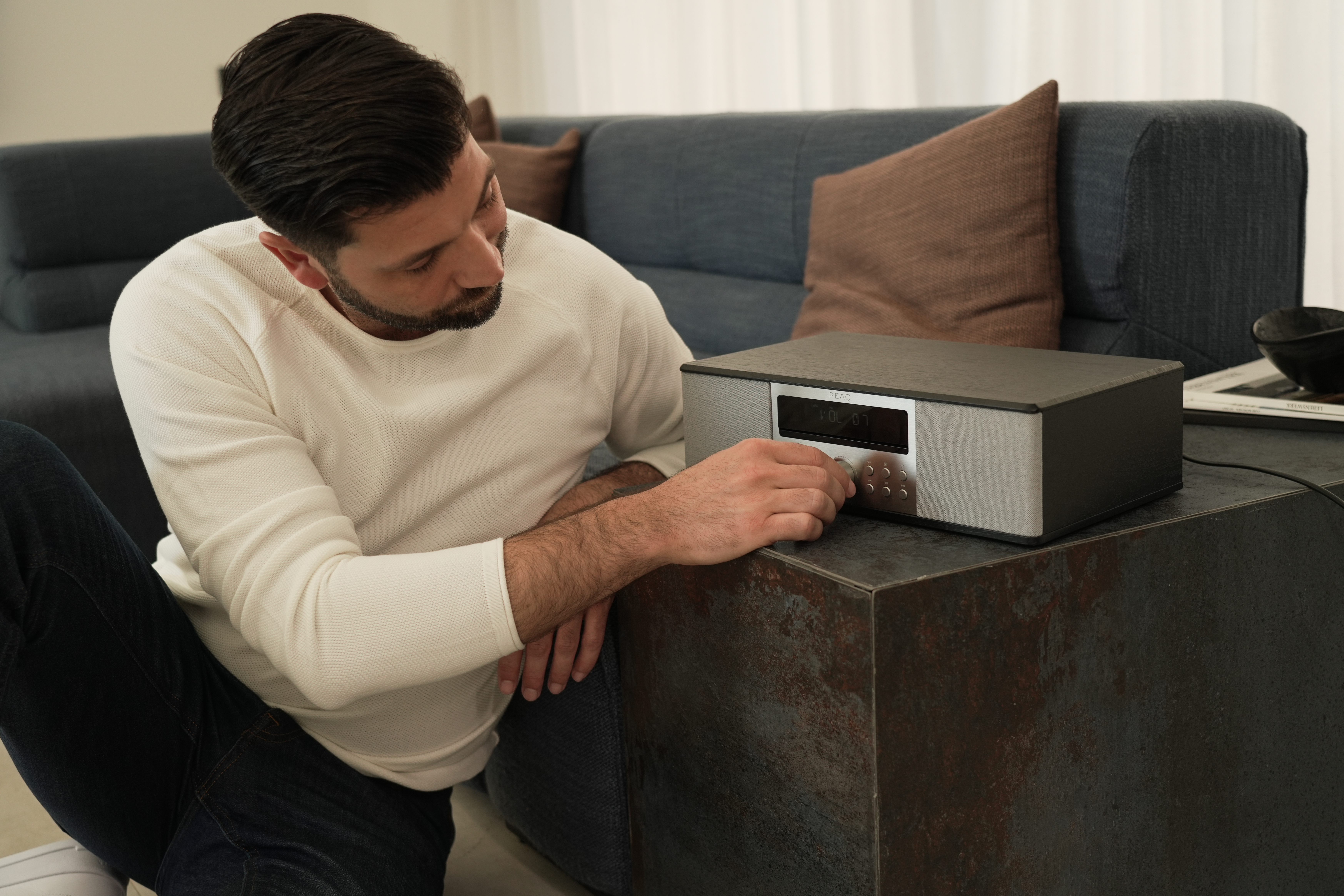 Ein Mann sitzt und bedient ein schwarz-silbernes Stereoanlage auf einem Tisch.