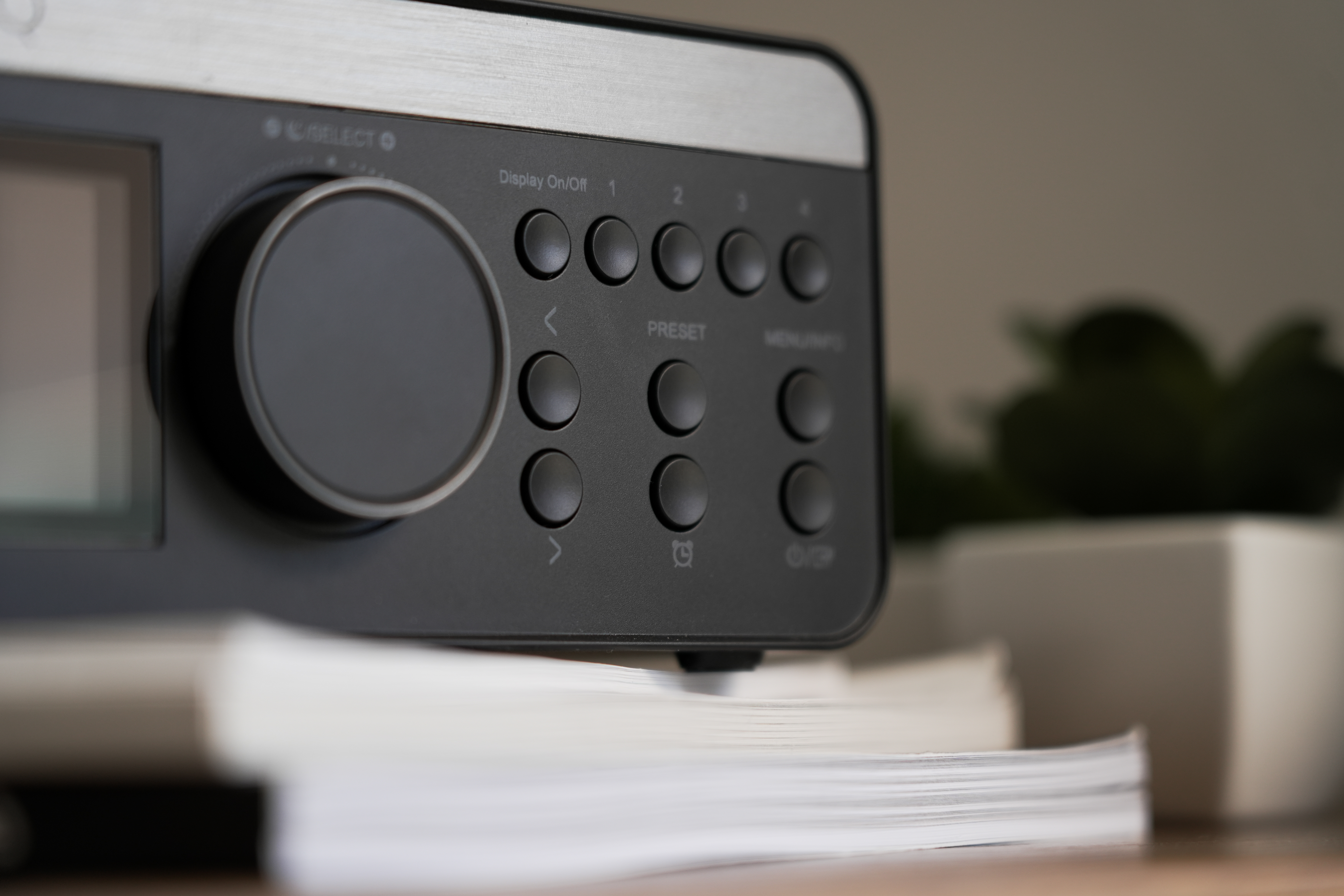 Radiogerät mit Knöpfen, Display und großem schwarzen Drehknopf, mit einem Bücherstapel.