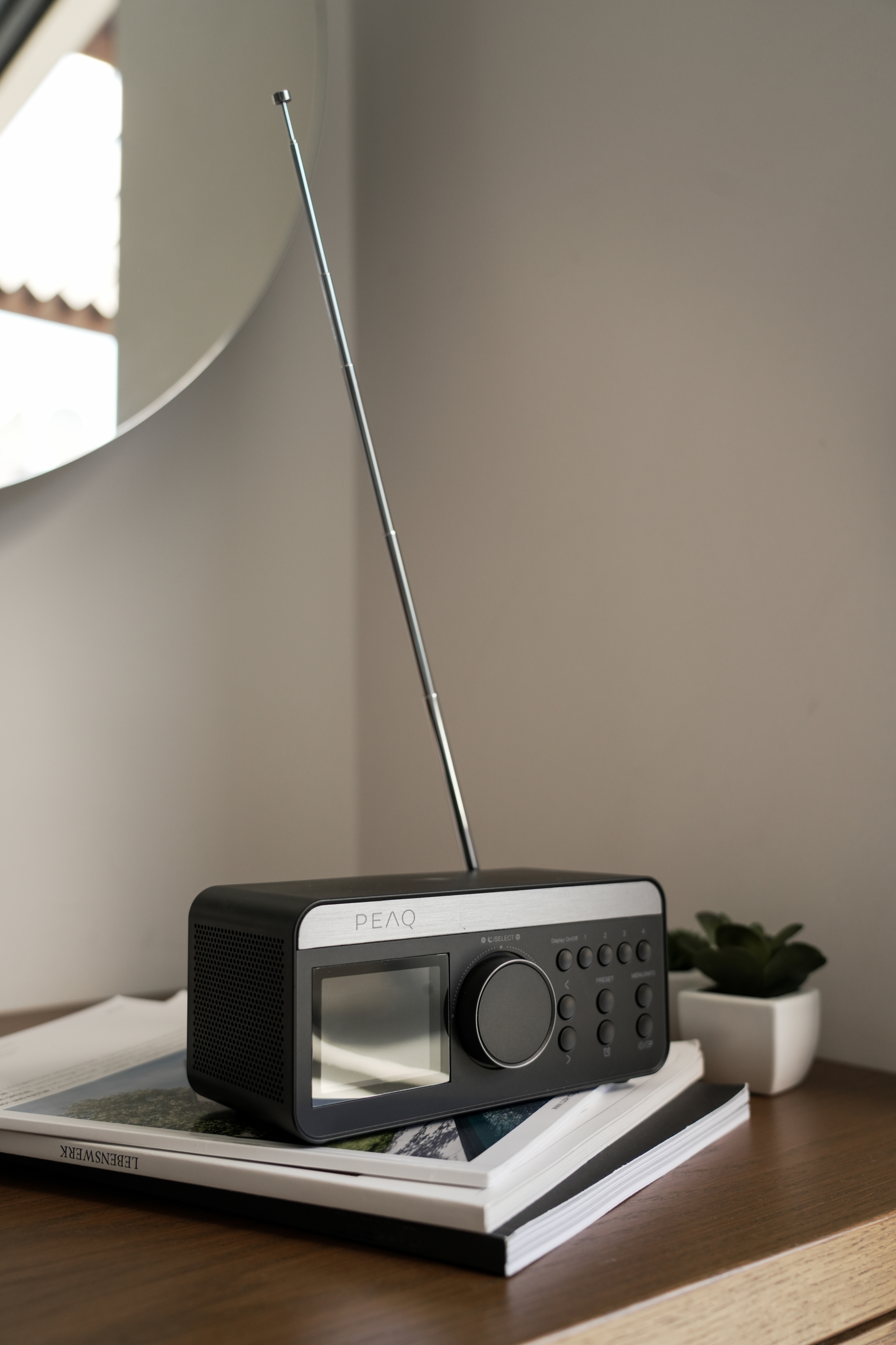 Schwarzes Radio mit Antenne auf Holztisch, vor weißer Wand und Spiegel.