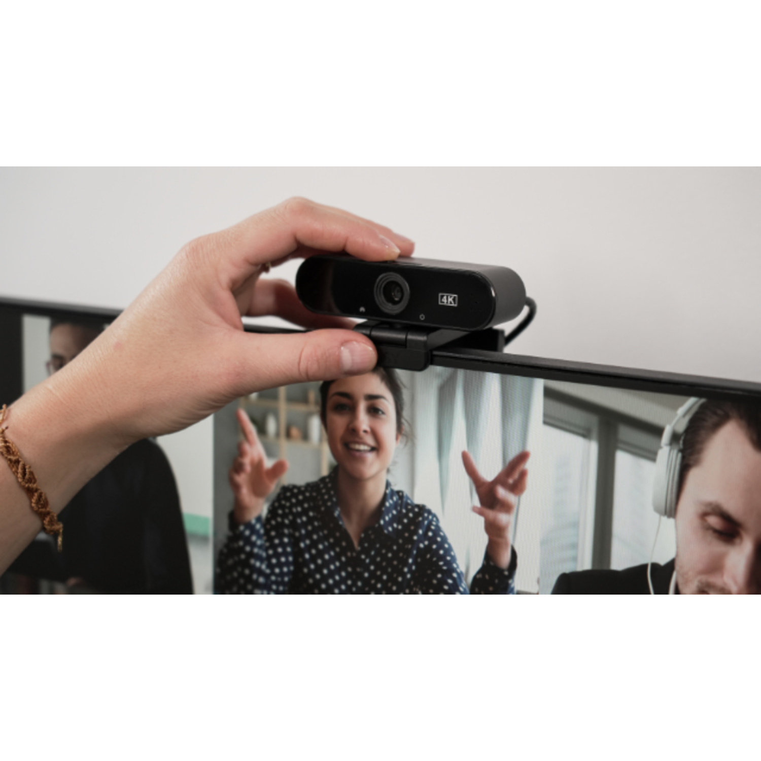 La main d'une personne ajustant une webcam noire montée sur le dessus d'un écran d'ordinateur.