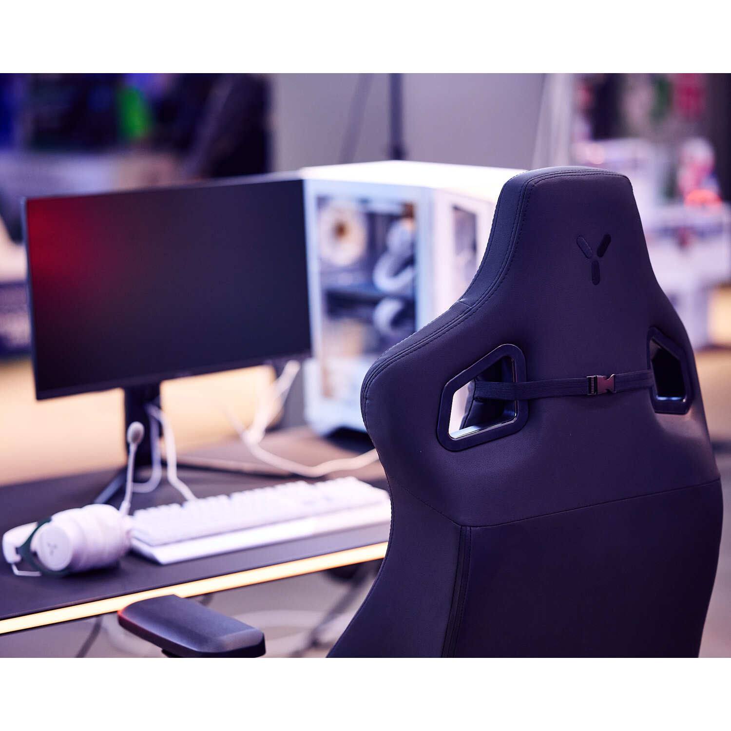 Gaming setup, zwarte stoel, bureau, monitor en pc. Wit toetsenbord en koptelefoon.
