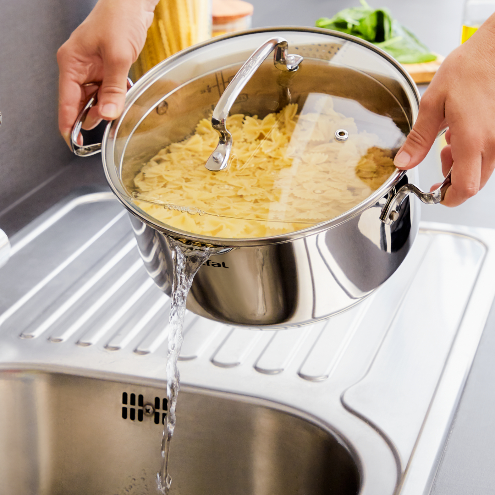 Osoba wylewa wodę z garnka z ugotowanym makaronem do zlewu. Garnek jest ze stali nierdzewnej.