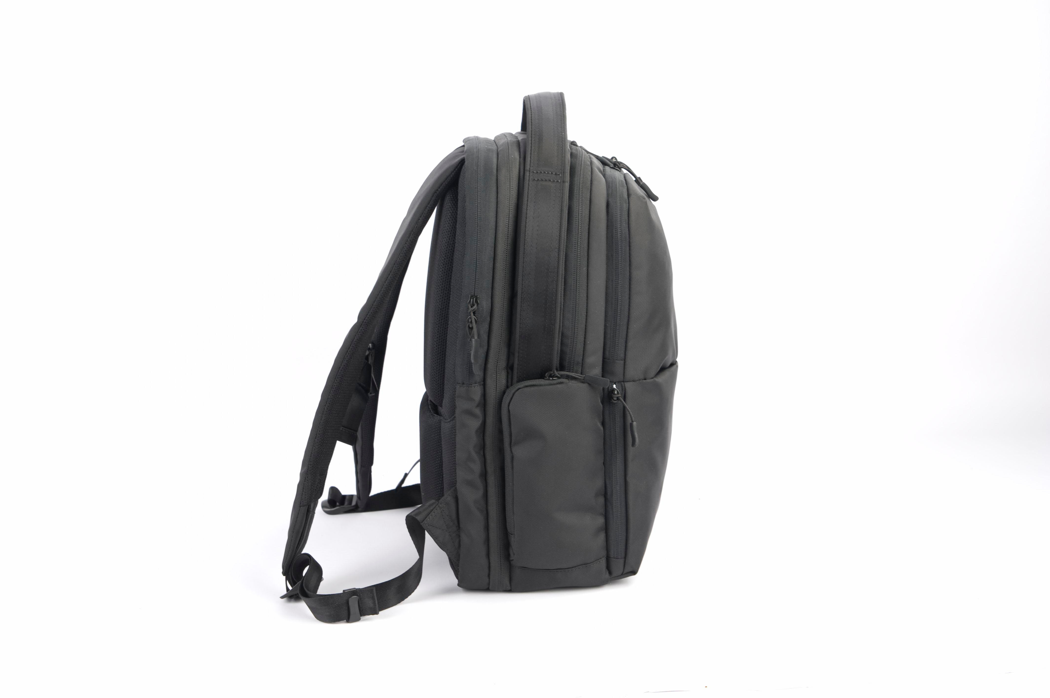 Schwarzer Rucksack von der Seite betrachtet, mit mehreren Taschen und Gurten, auf weißem Hintergrund.