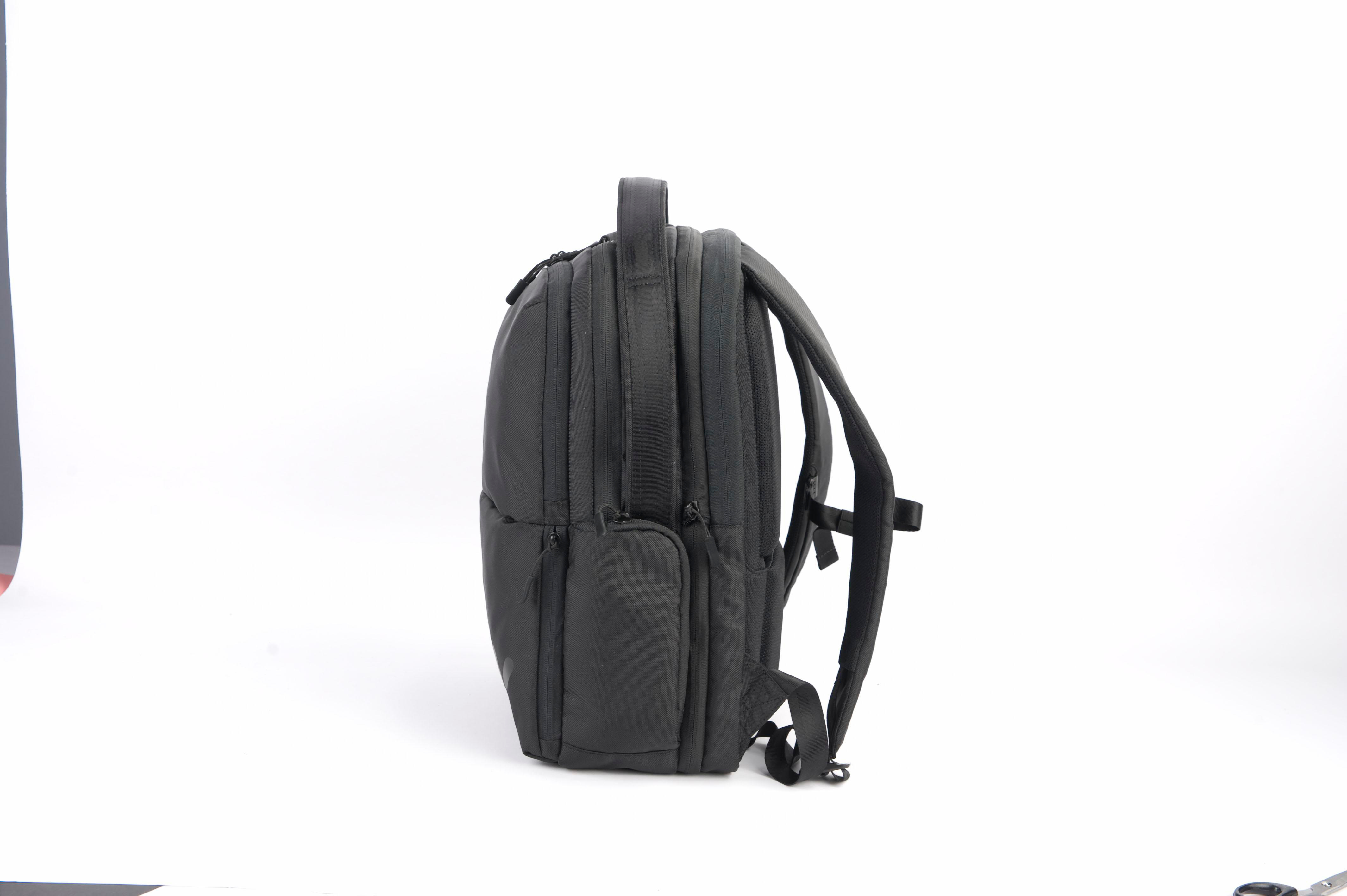 Ein schwarzer Rucksack, Seitenansicht, mit Henkel oben, auf weißem Grund.