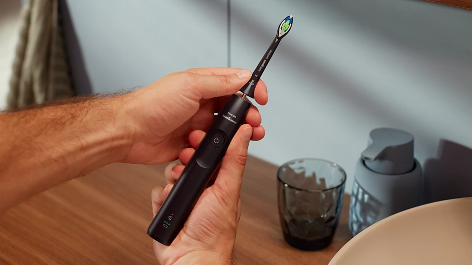 Hände halten eine schwarze Philips Sonicare Zahnbürste.