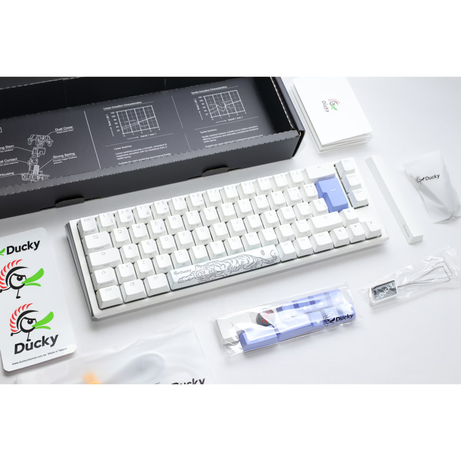 Un teclado Ducky blanco con varios accesorios sobre una superficie blanca.