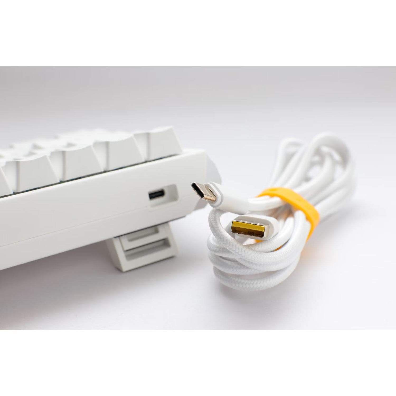 Teclado blanco con cable USB-C conectado, fondo blanco.