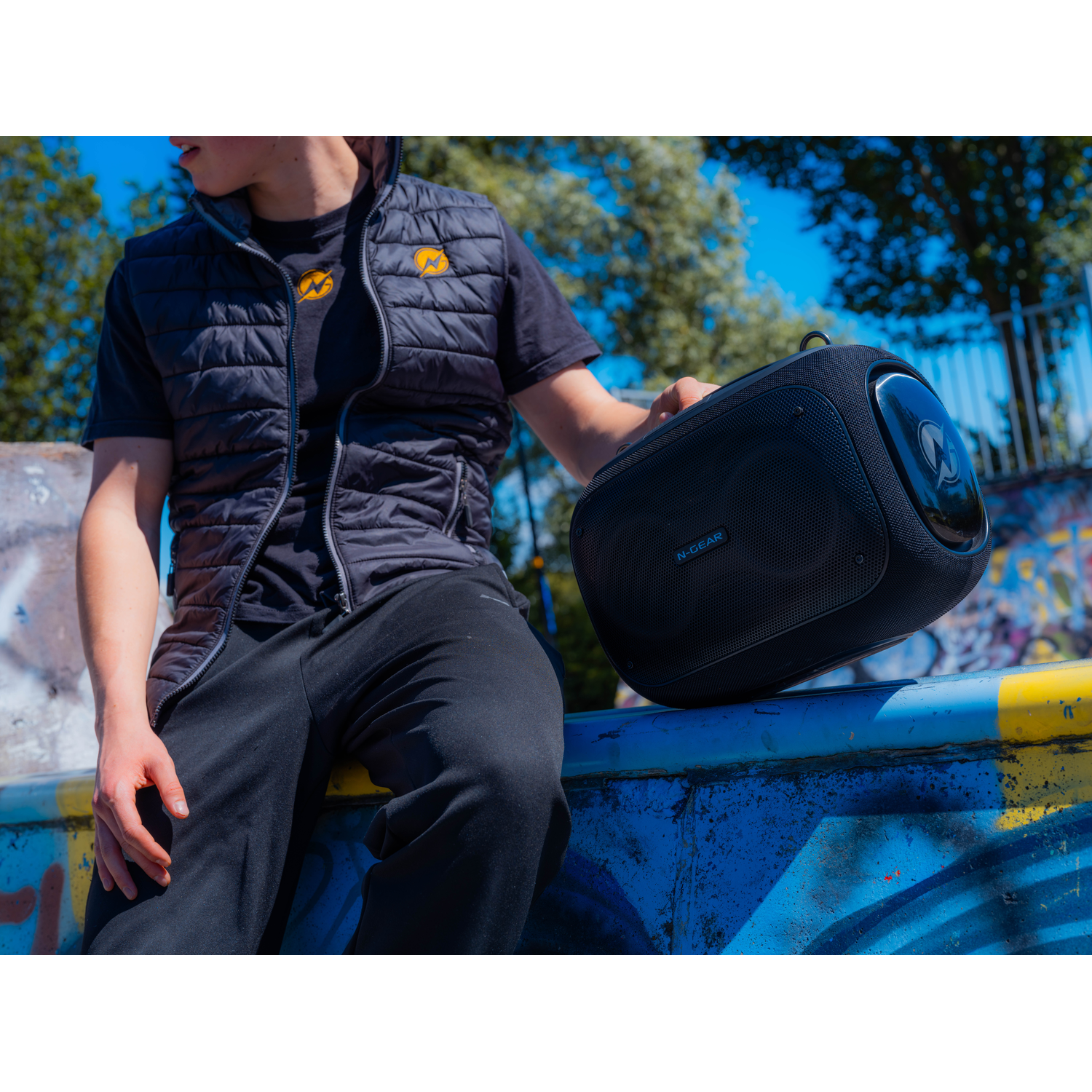 Man holding a black speaker on a blue and yellow painted background.