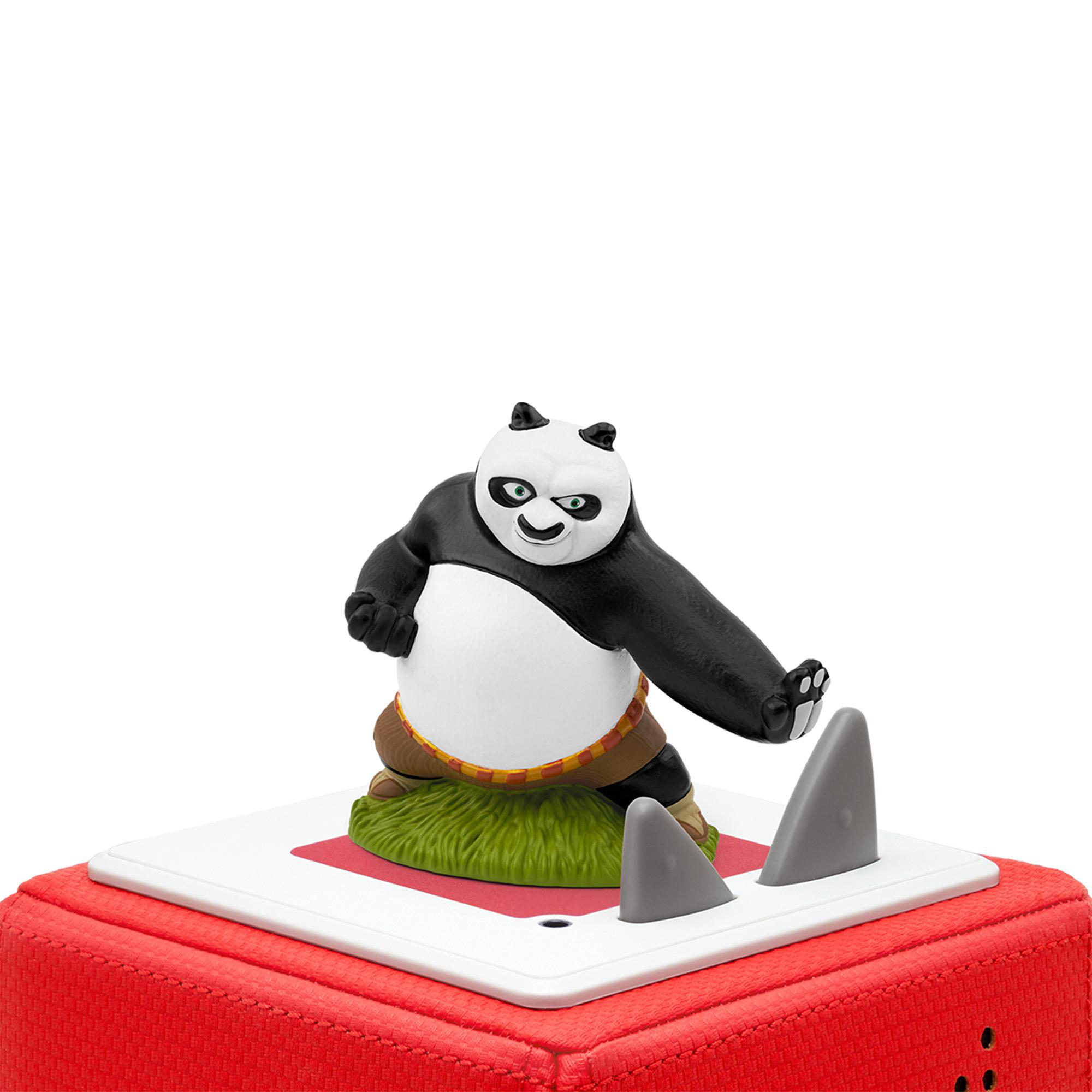 Kung Fu Panda Figur auf rotem Würfel mit Haifischflossen. Panda steht auf Gras, weißer Hintergrund.