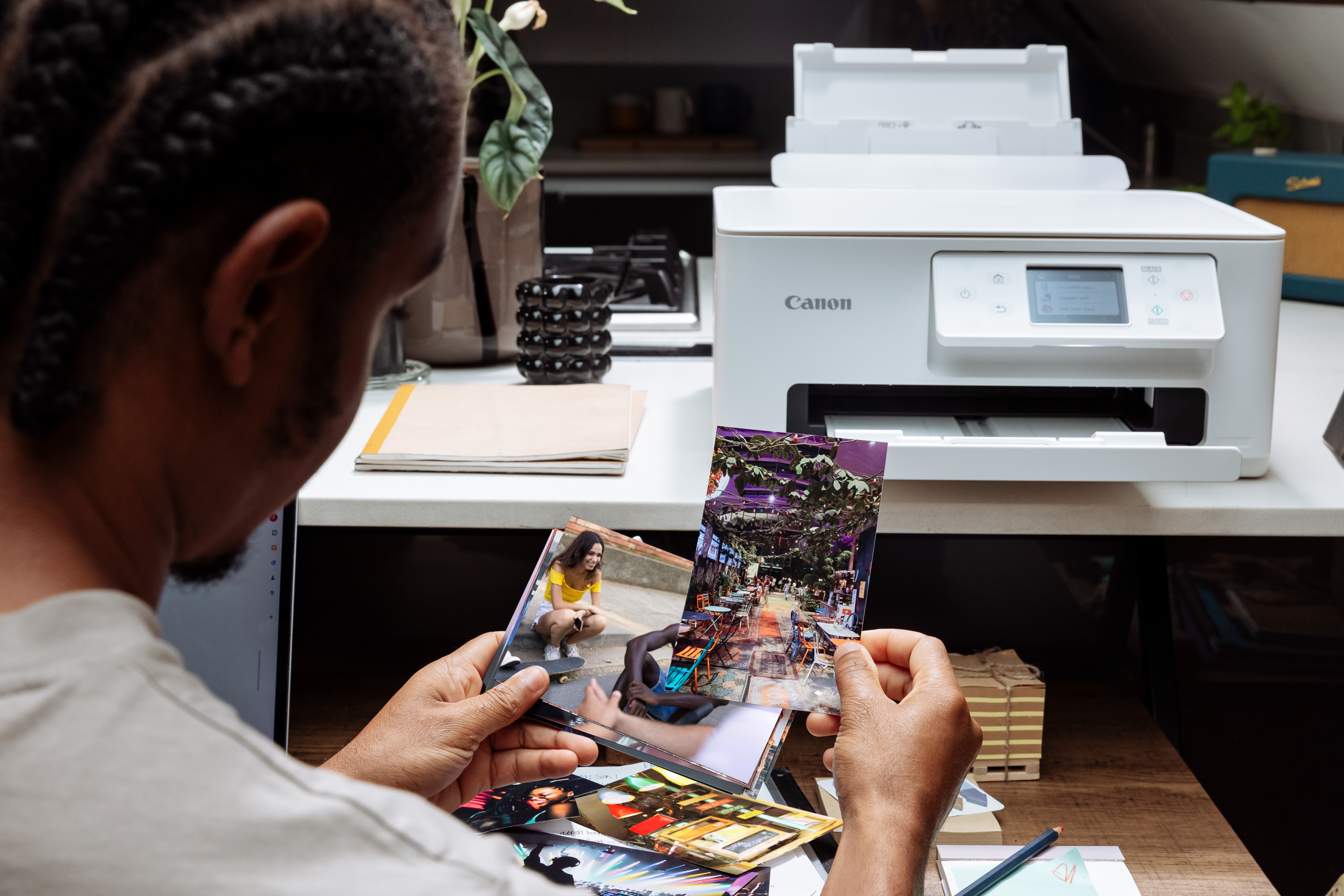 Person betrachtet Fotos, die von einem Canon-Drucker gedruckt wurden. Drucker und Schreibtischartikel sind sichtbar.