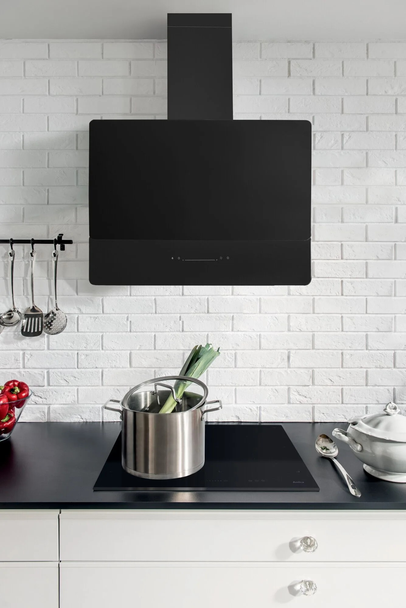 Kuchnia z czarnym okapem, garnkiem z porami i białą ceglaną ścianą.