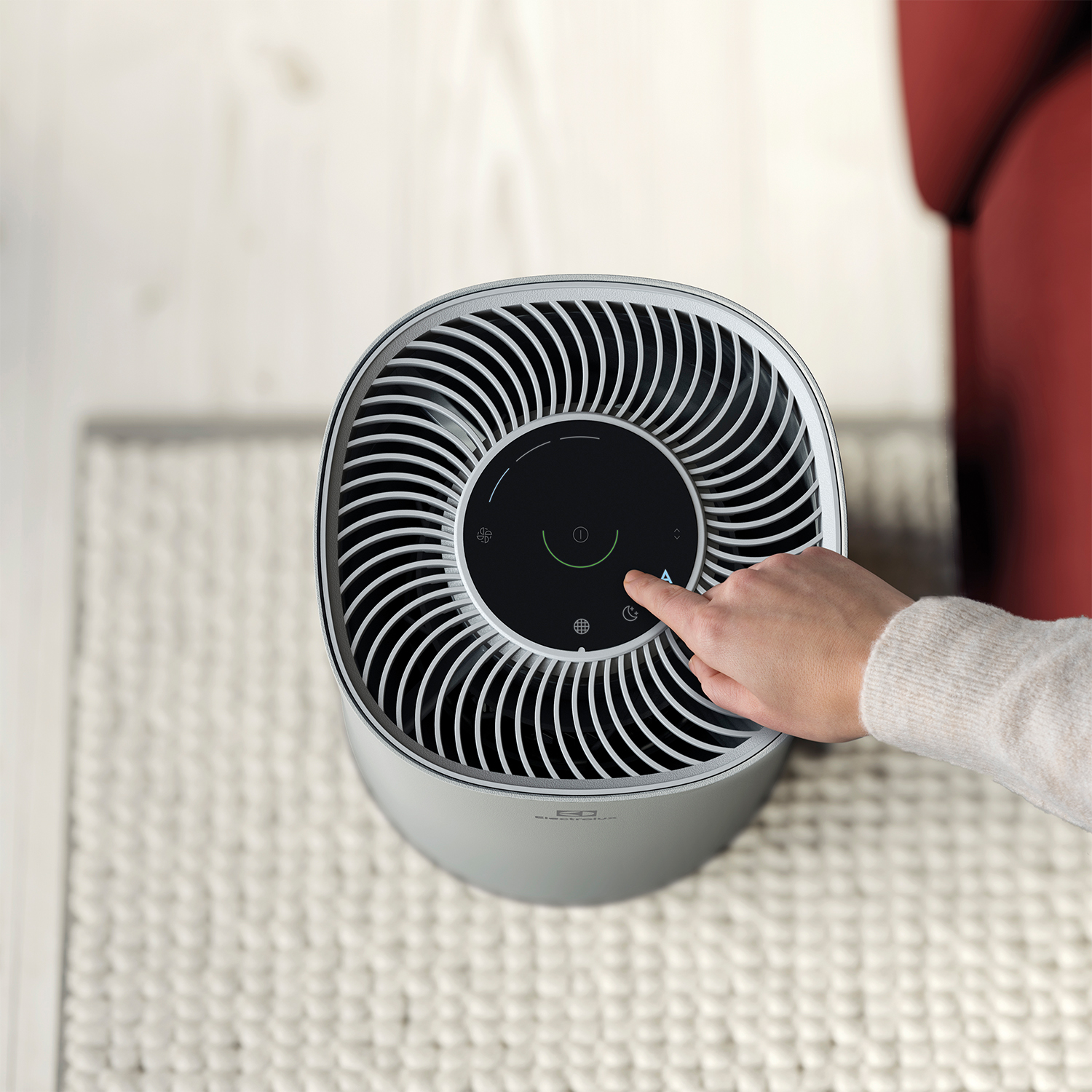 Una mano preme un pulsante su un purificatore d'aria bianco e grigio. È su un tappeto bianco.