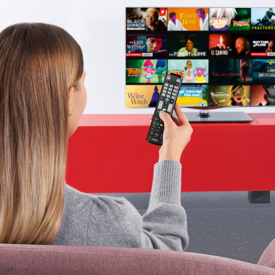 Una mujer sostiene un mando a distancia y ve la televisión. El televisor muestra títulos de películas.