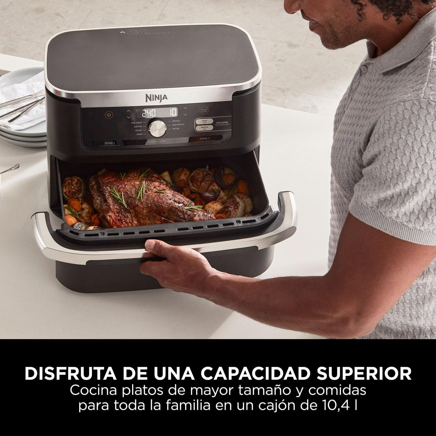 Freidora de aire Ninja negra con comida dentro. Manos del hombre sosteniendo la bandeja. Texto: Disfruta mayor capacidad.
