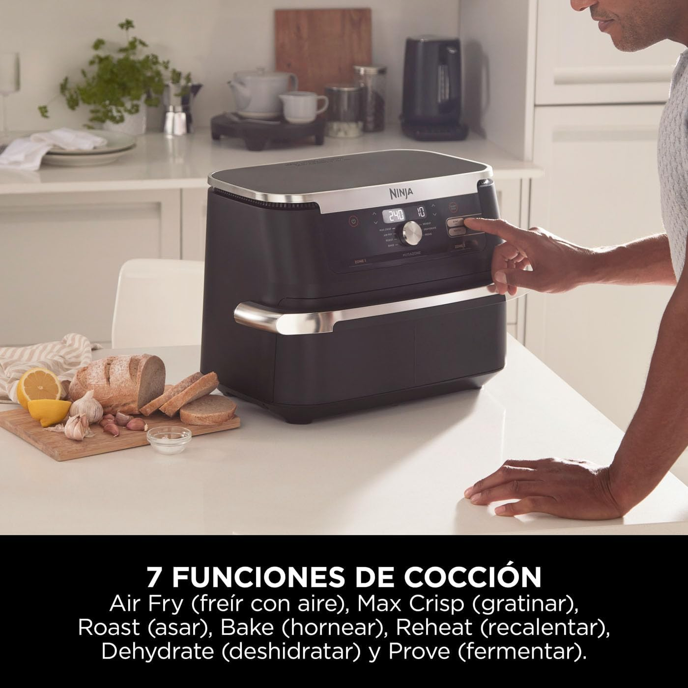 La mano de una persona presiona un botón en una freidora de aire negra. Comida en la encimera delante.