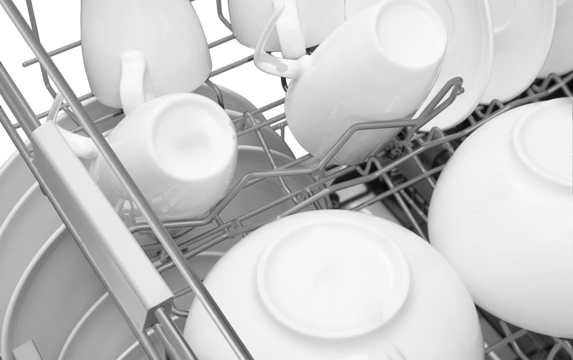 Zbliżenie w skali szarości na wnętrze zmywarki z białymi naczyniami, kubkami i miskami w stojakach.