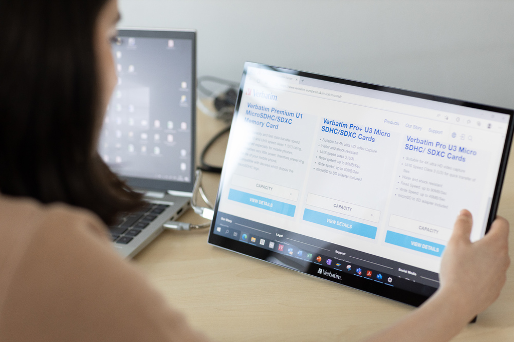 Eine Person verwendet einen tragbaren Monitor, auf dem eine Verbatim-Website angezeigt wird, mit einem Laptop in der Nähe.