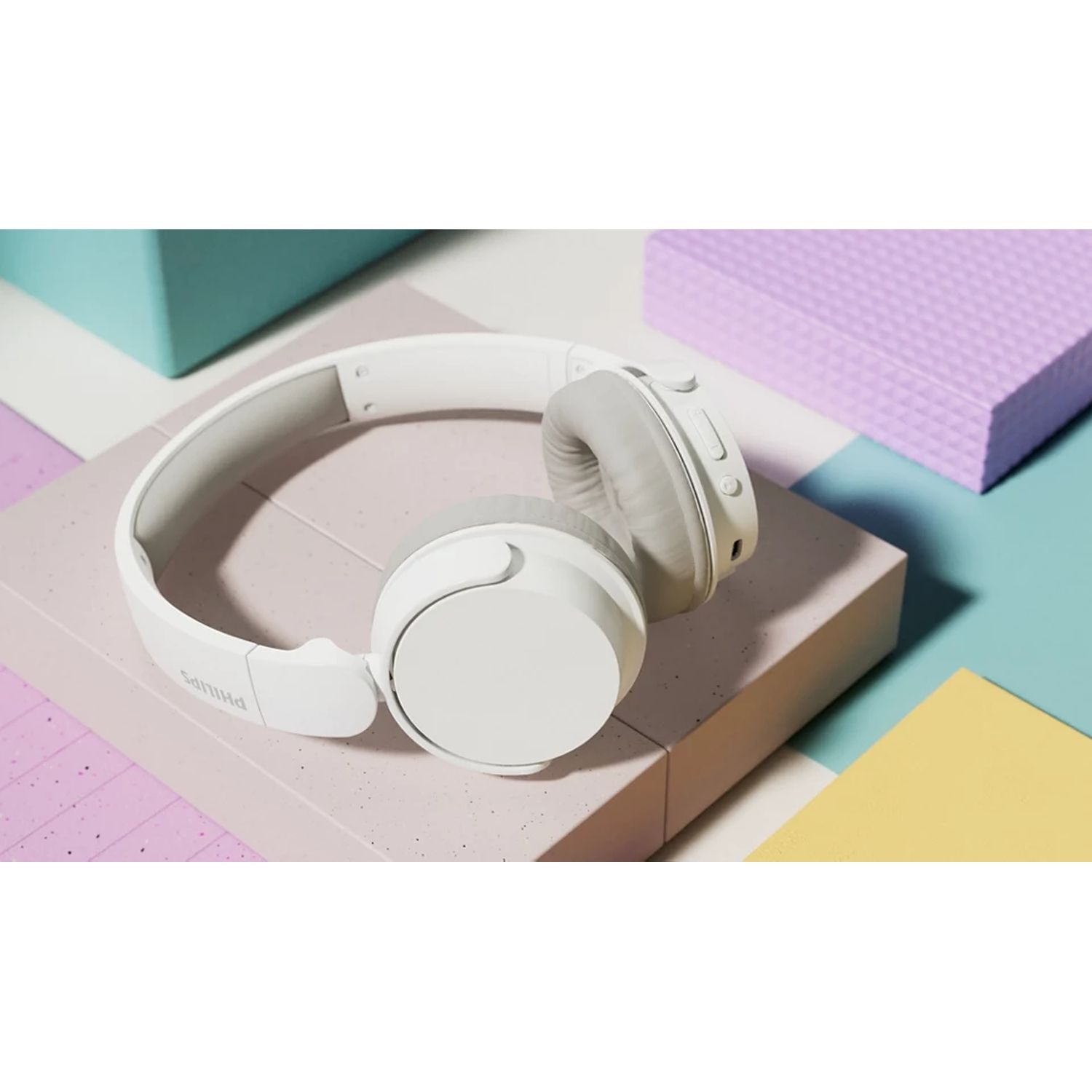 White Philips headphones on a pink and blue surface with a purple box in the background.