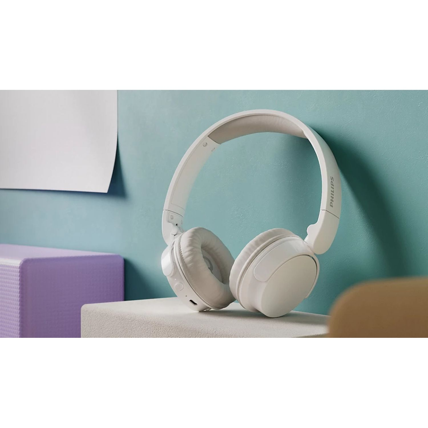 White headphones on a light blue surface. A purple block is next to the headphones.