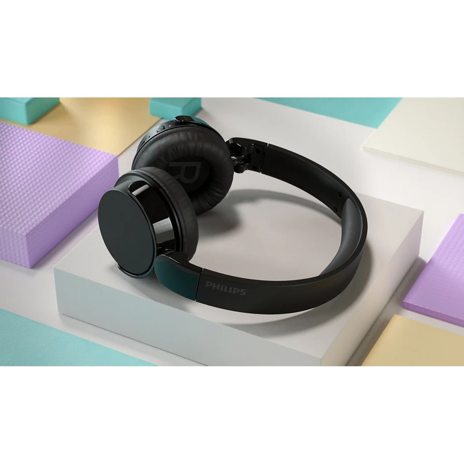 Black Philips headphones on a white block with colorful background.