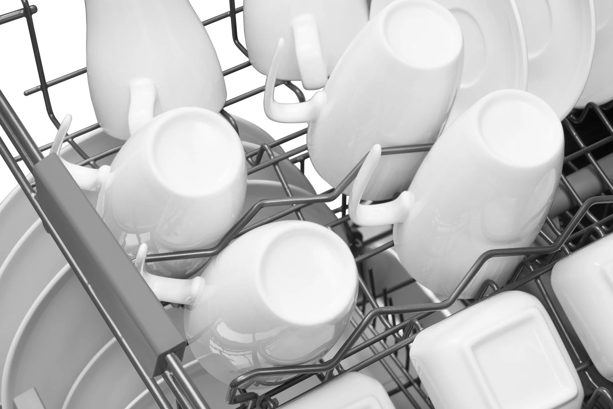 W zmywarce białe kubki i talerze ułożone są na stojakach.