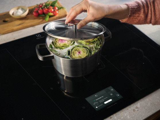 Osoba nakłada pokrywkę na garnek ze stali nierdzewnej z karczochami na płycie grzejnej.