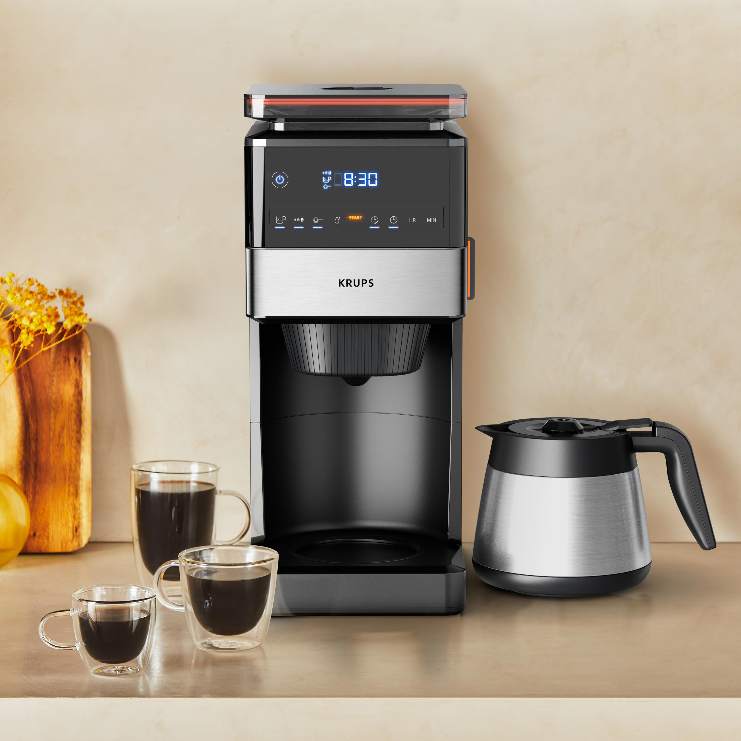Kaffeemaschine mit zwei Kaffeetassen, einer Karaffe und Zeitanzeige 8:30. Gelbe Blumen auf einem Holzbrett.