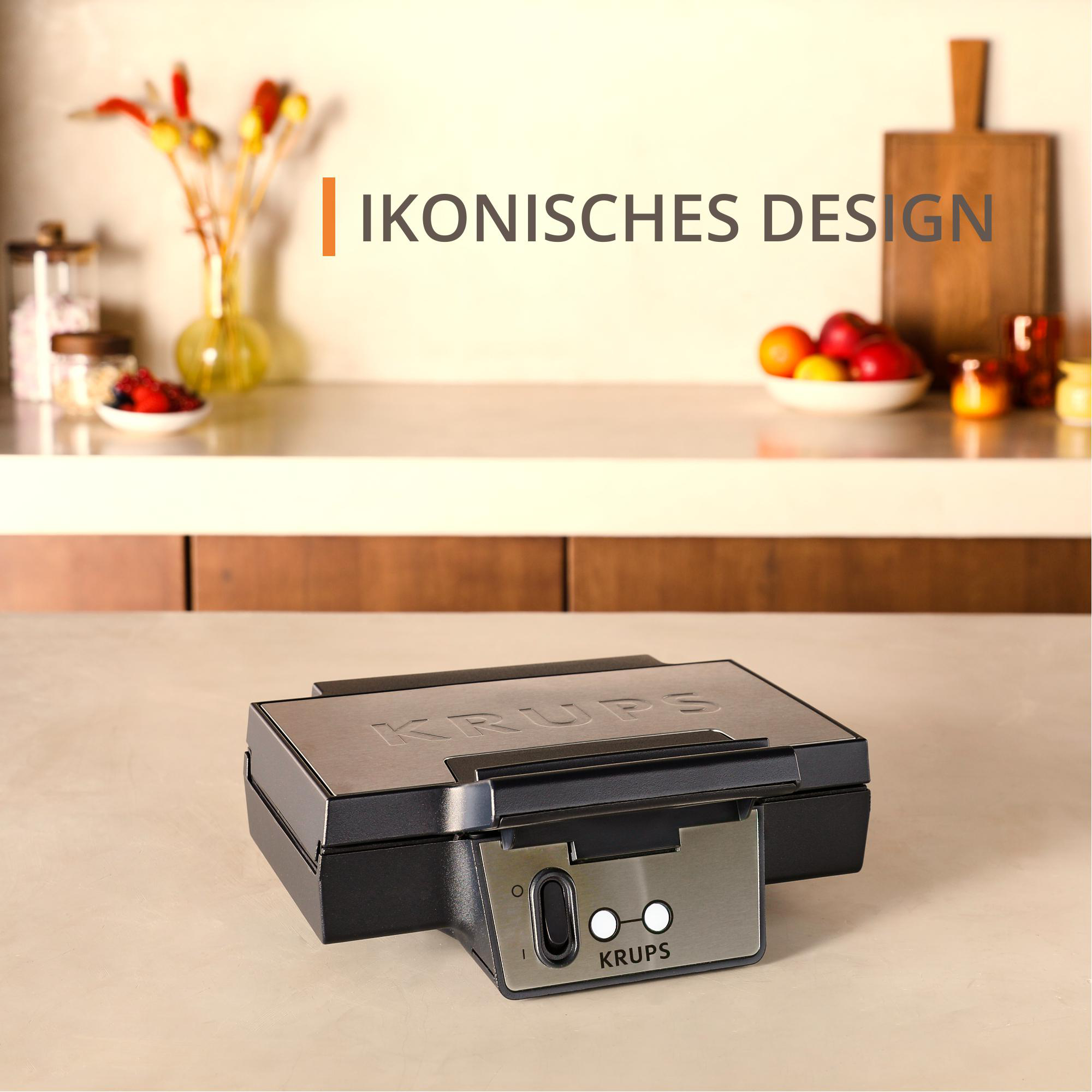 Krups-Waffeleisen auf einer Arbeitsplatte, mit dem Text: IKONISCHES DESIGN. Das Waffeleisen ist schwarz und metallisch.