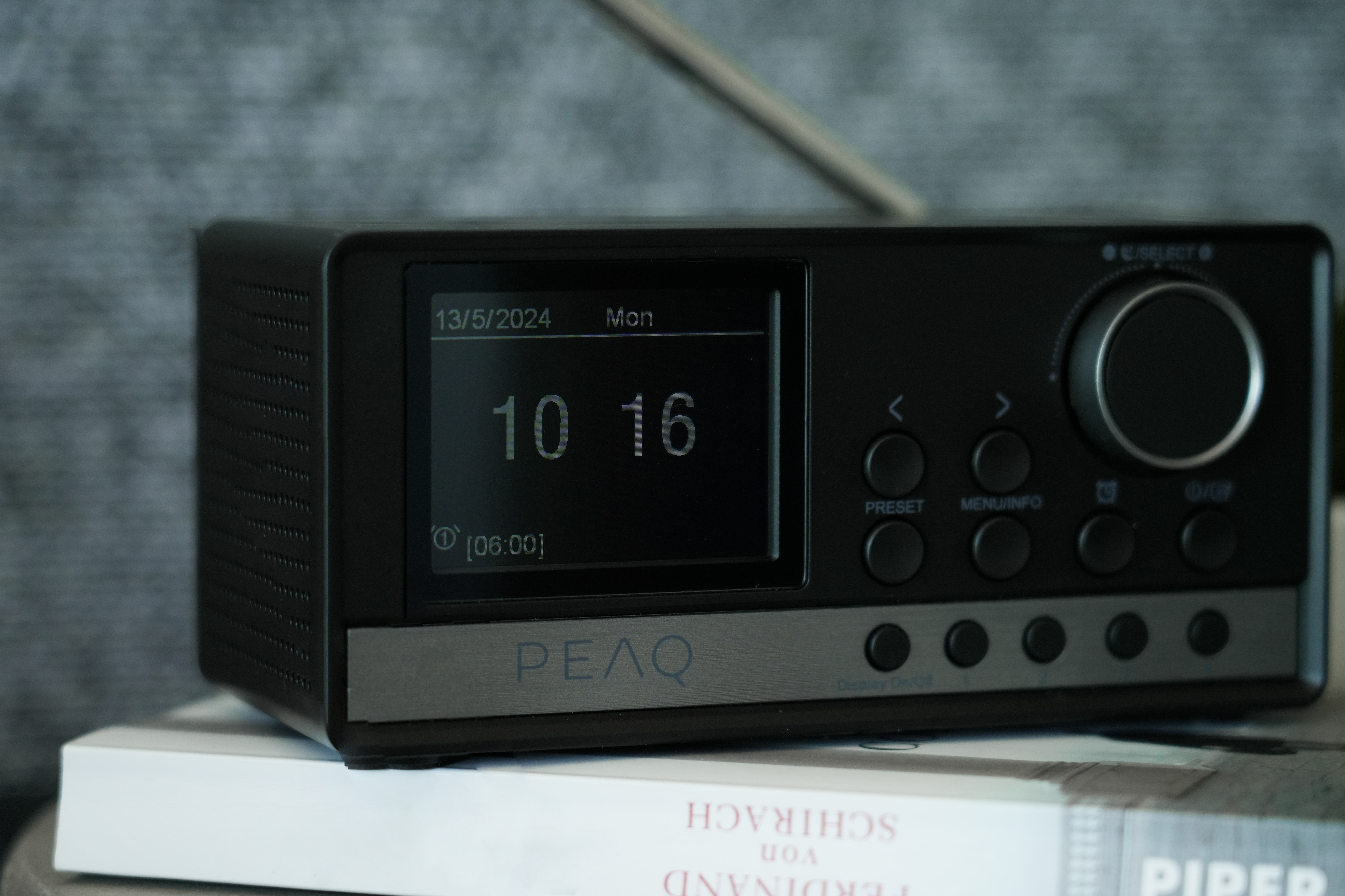 Schwarze Funkuhr auf einem Buch, zeigt Zeit und Datum, mit Steuertasten.