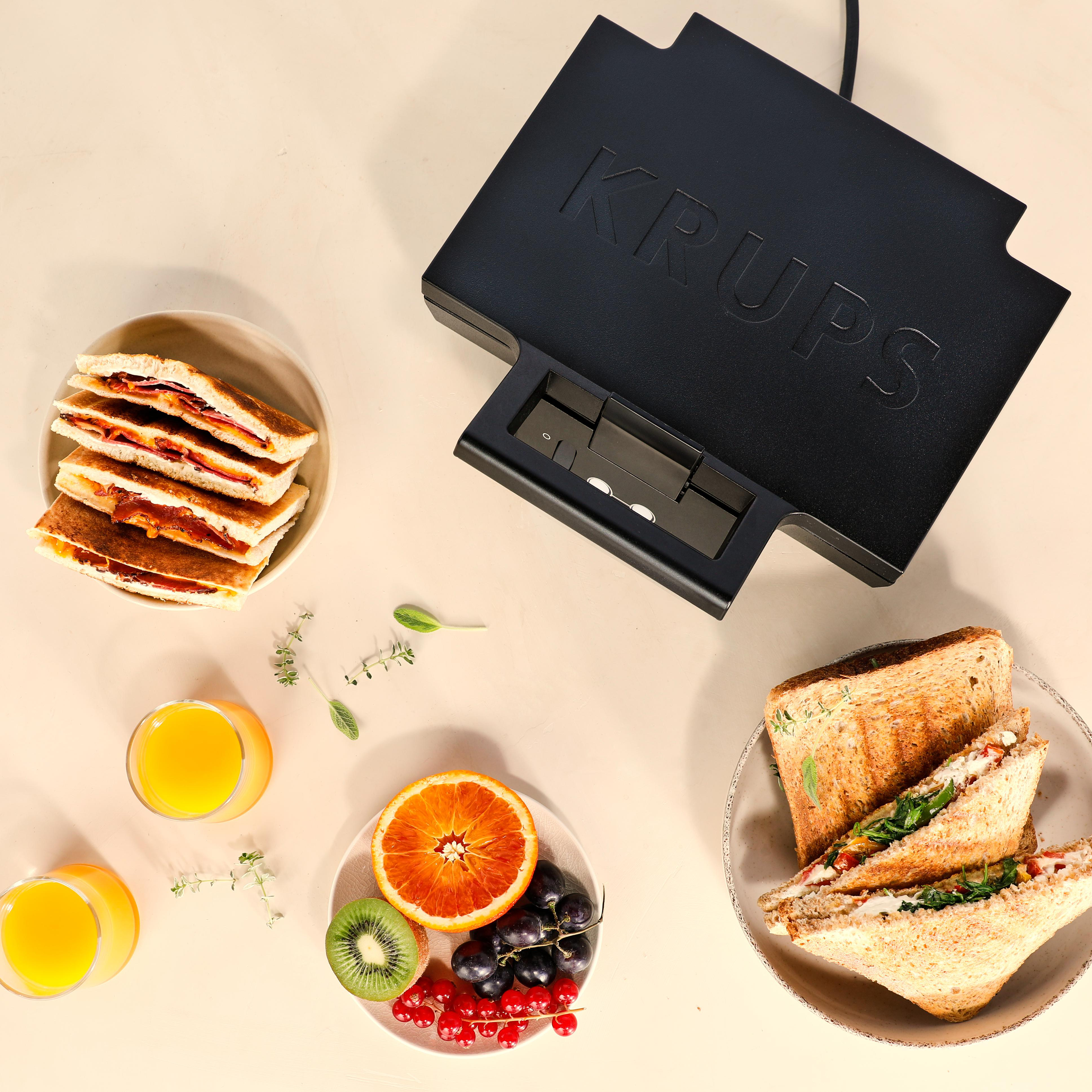 Sandwichmaker mit zwei Tellern Sandwiches, Obst und Orangensaft.