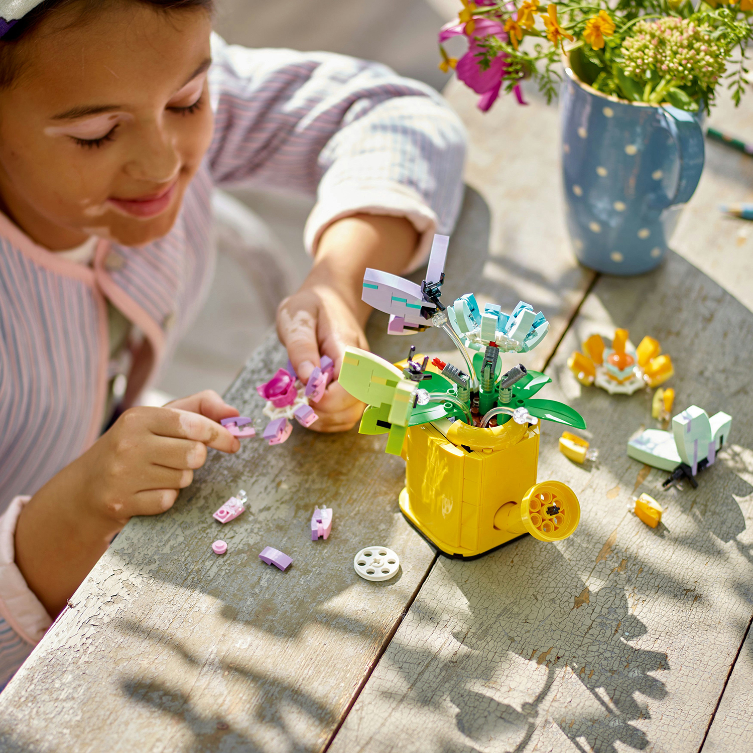 Una bambina costruisce con i LEGO. Fiori LEGO e un carretto giallo su un tavolo di legno.