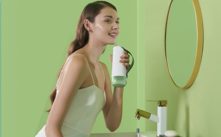 Kobieta używająca białego i zielonego irygatora w łazience z zieloną ścianą i złotym lustrem.