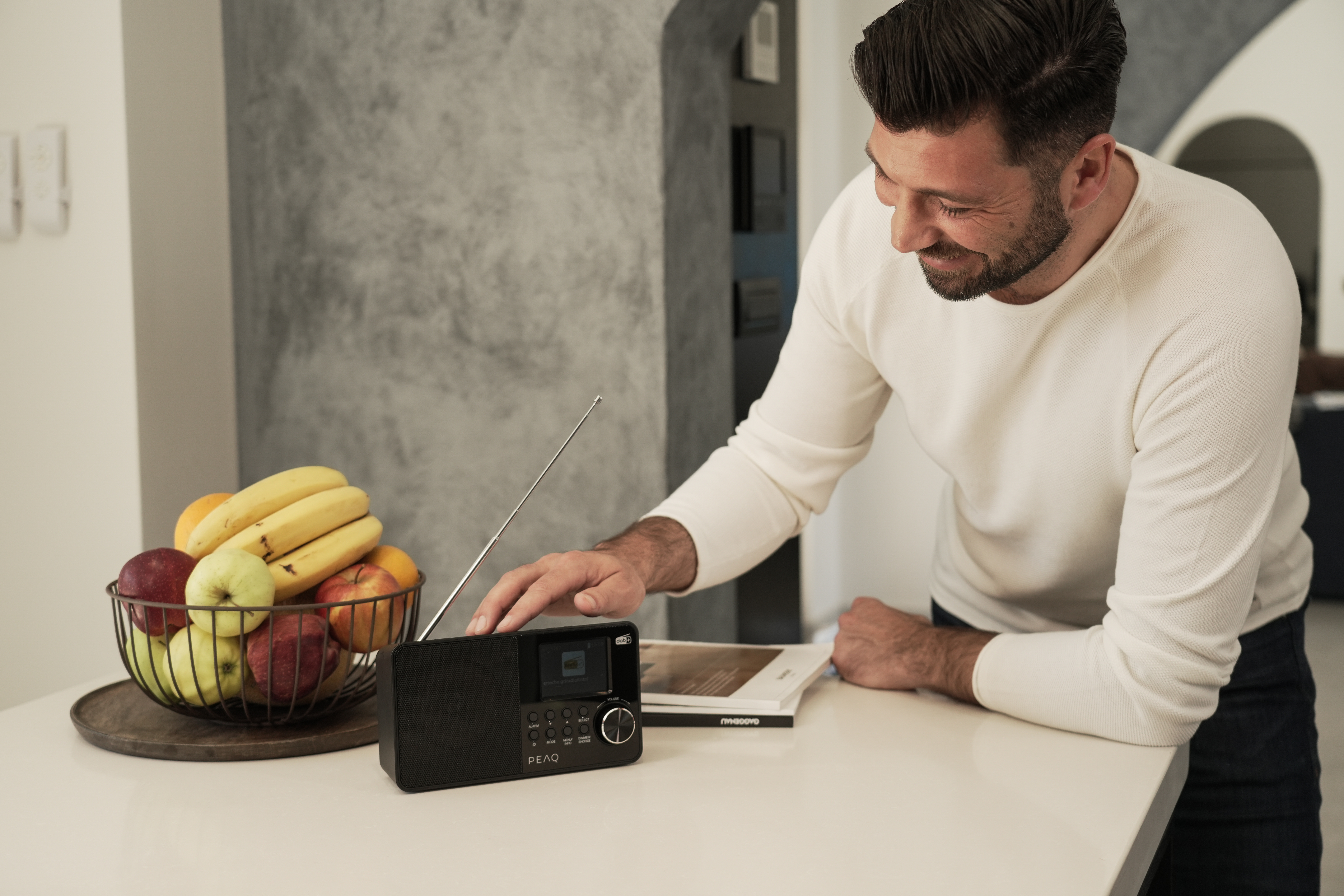Mann lächelt, berührt ein schwarzes Radio auf einer weißen Arbeitsplatte mit Obst.