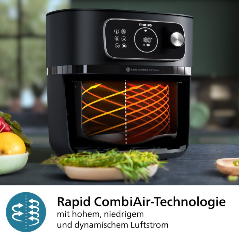 Friteuse à air Philips noire avec vue vitrée montrant l'intérieur et des légumes à côté.