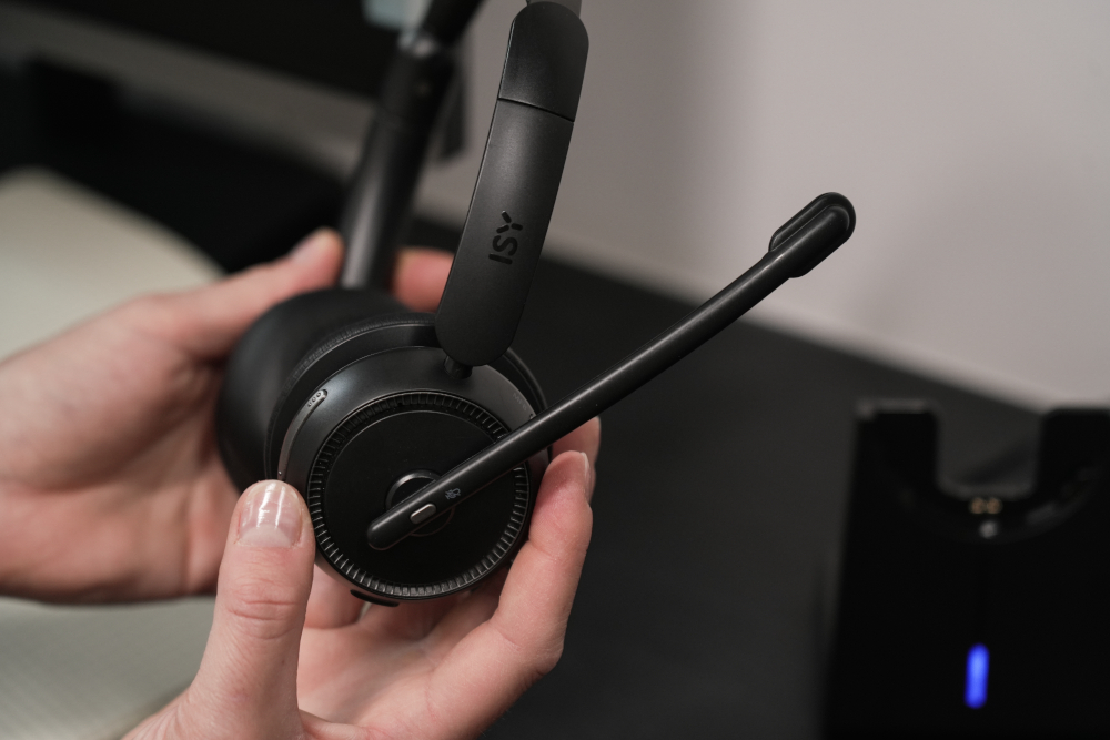 A person holding a black headset with a microphone and charging station.