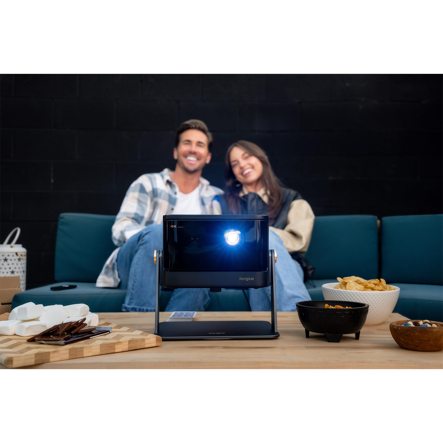 Coppia che guarda un film con proiettore su un tavolo con snack e sfondo nero.