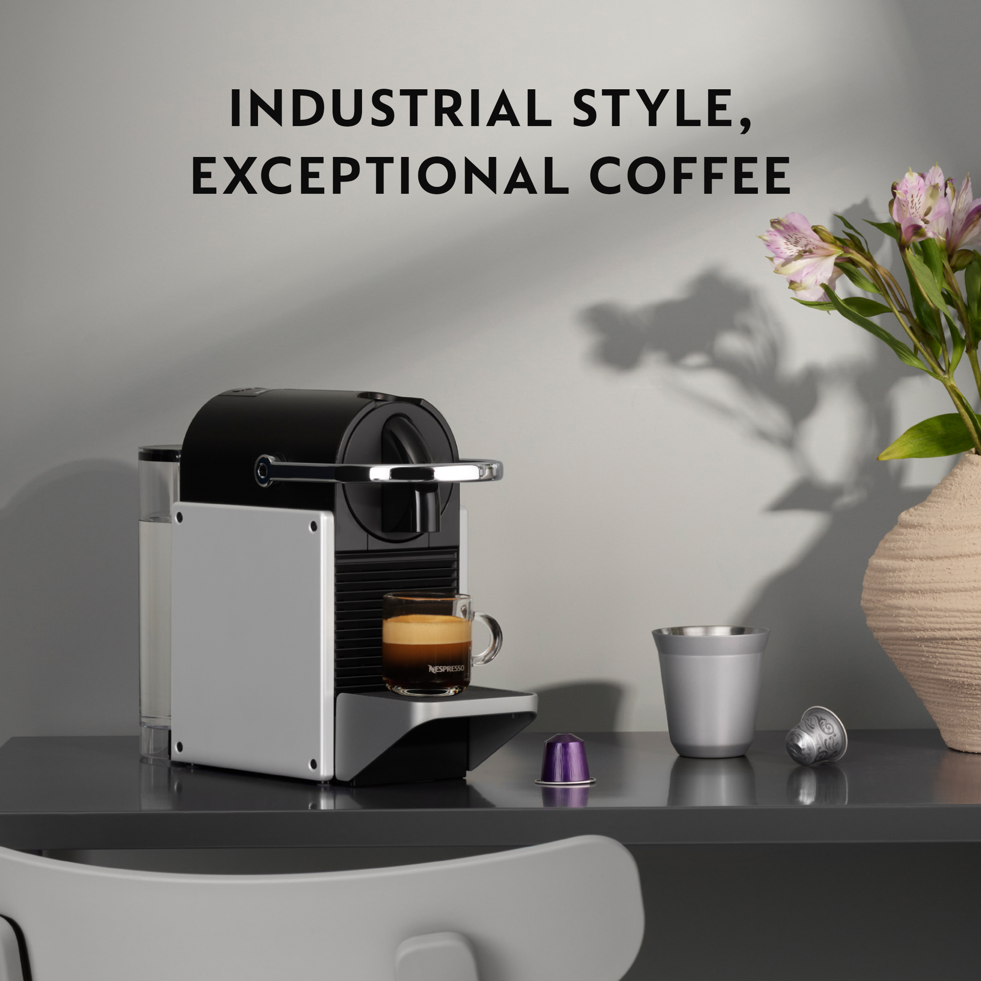 Nespresso-Kaffeemaschine mit Tasse. Kaffee wird eingegossen, neben einer Tasse und Kapseln.