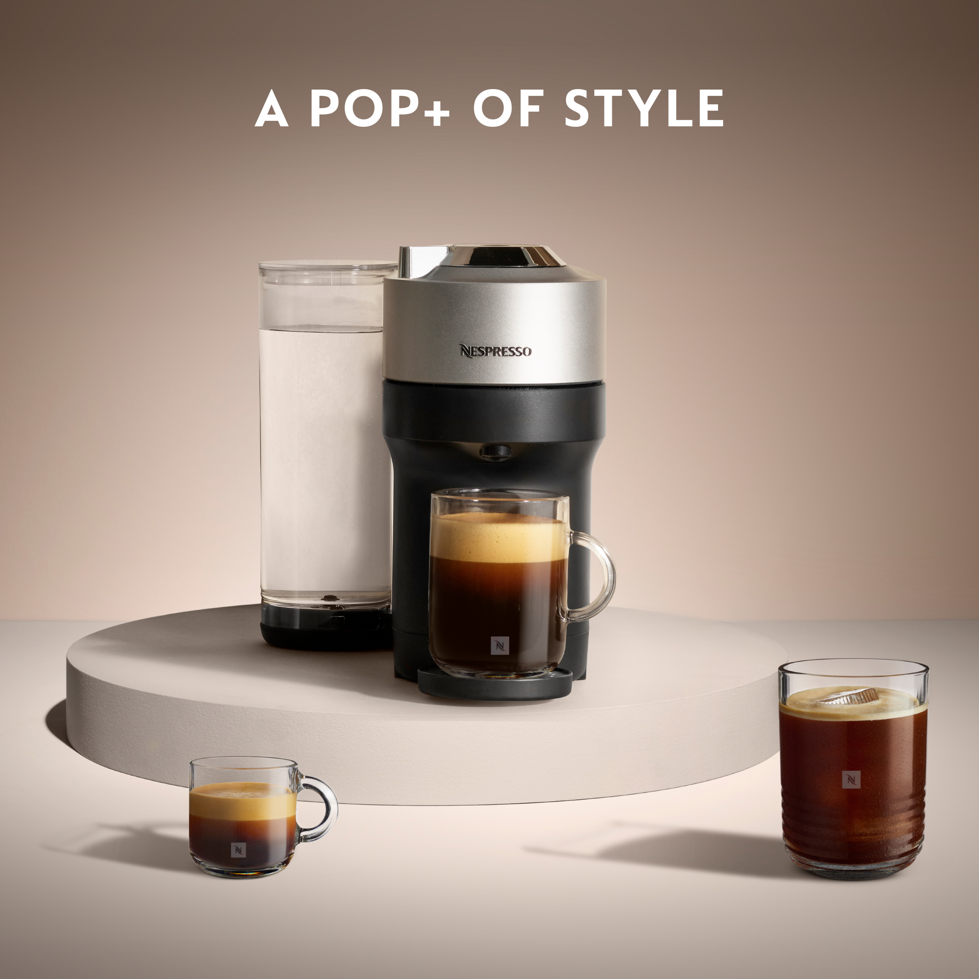 Macchina Nespresso con tazze. Il testo dice 'A POP+ OF STYLE'. Una tazza è trasparente, altre espresso.