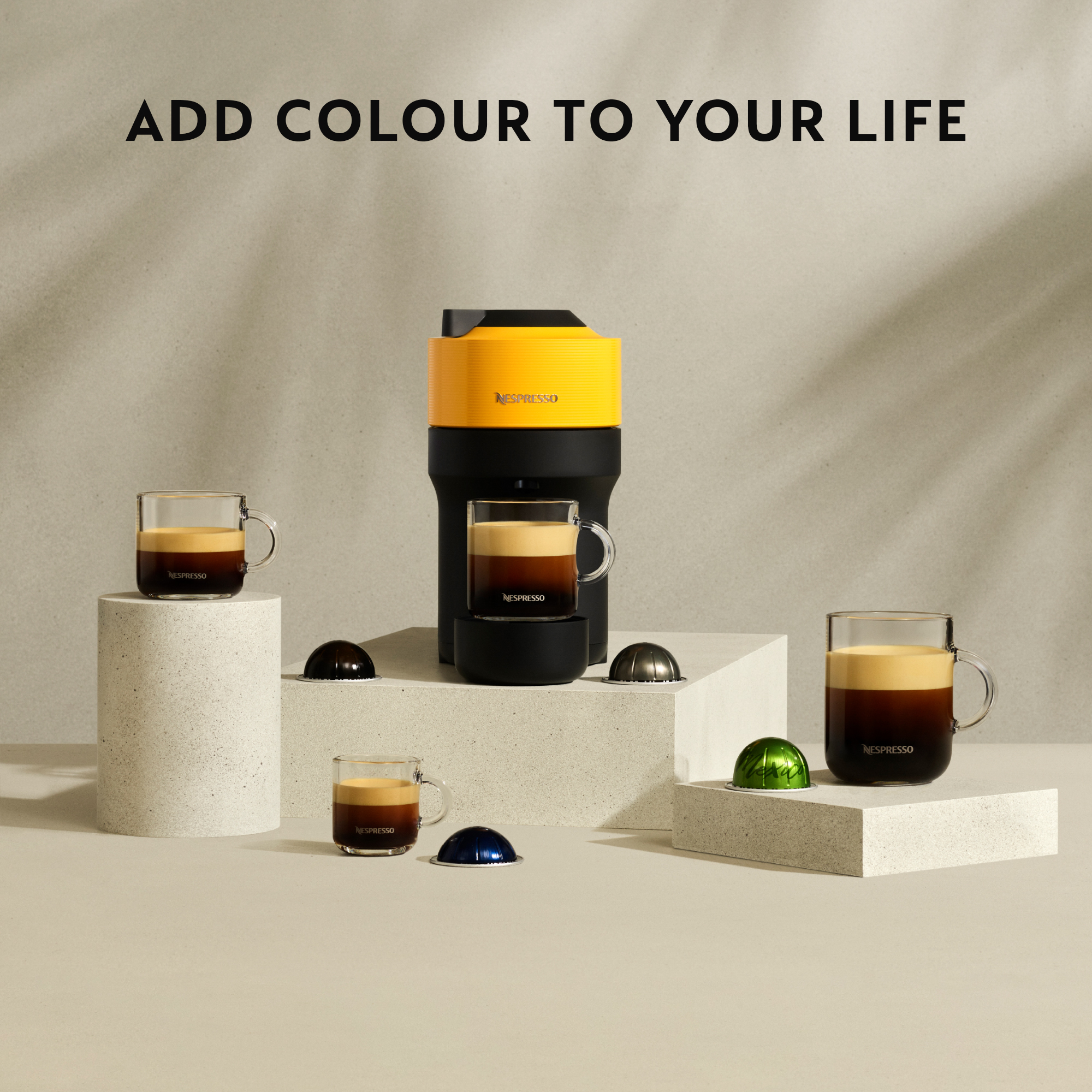 Eine Kaffeemaschine mit Kaffee in Gläsern auf weißen Plattformen. Nespresso-Kapseln liegen herum.