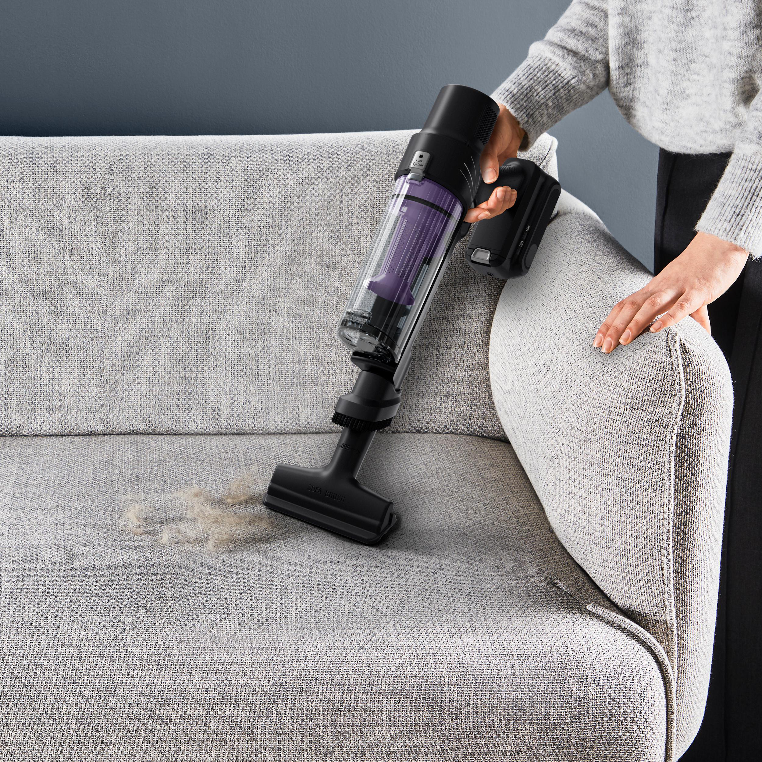 Eine Person benutzt einen Handstaubsauger auf einem Sofa.