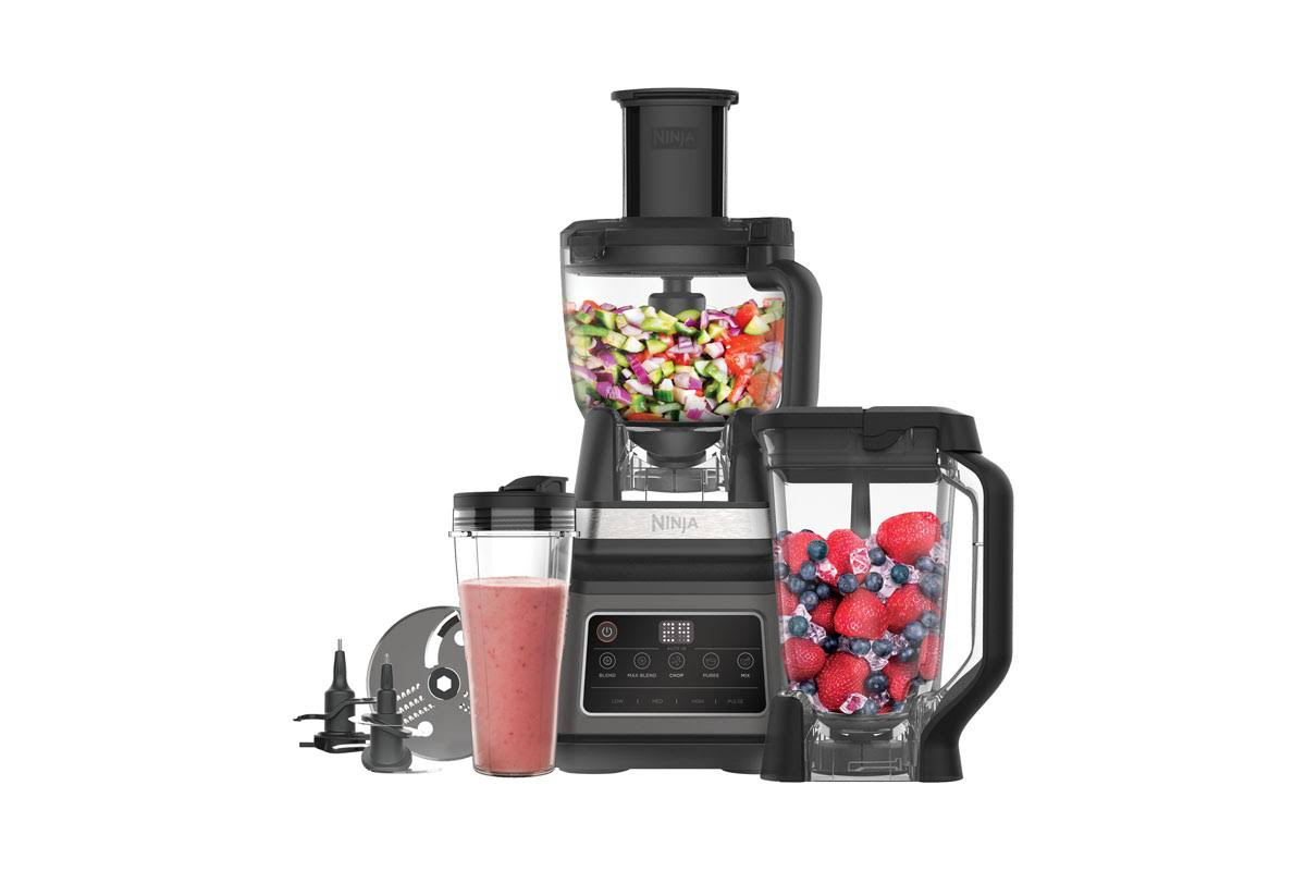 Una licuadora Ninja negra con un recipiente de verduras picadas, bayas y un batido.