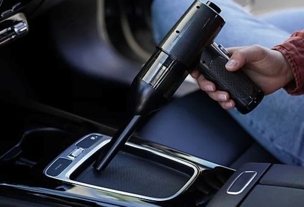 Osoba używająca czarnego odkurzacza ręcznego w samochodzie do czyszczenia konsoli środkowej.
