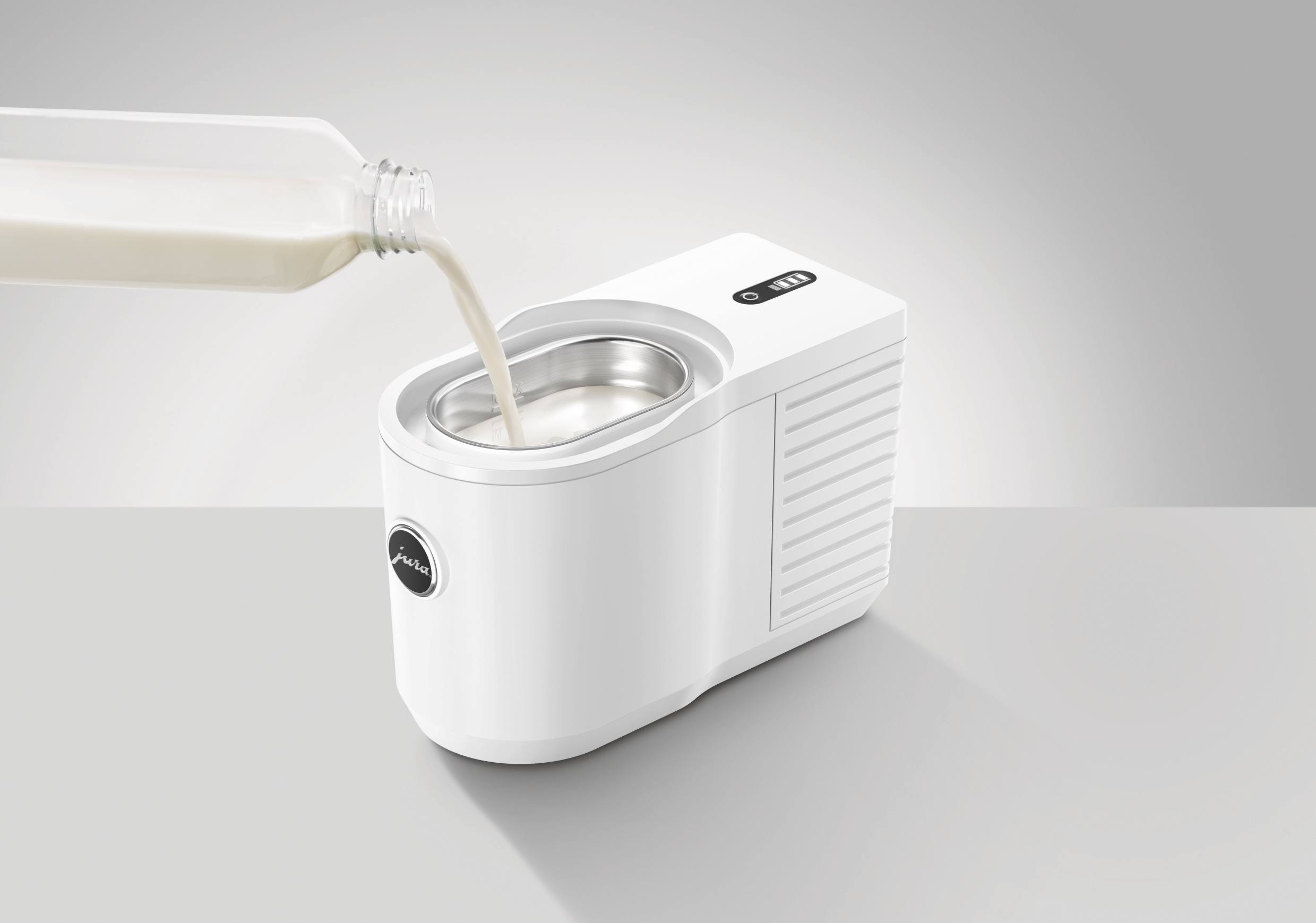 Milch wird in einen weißen Jura Milchaufschäumer gegossen. Das Gerät steht auf einer grauen Oberfläche.