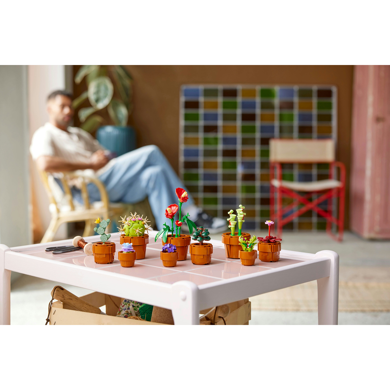 Piante grasse Lego su un tavolo rosa. Una persona sullo sfondo è seduta su una sedia.