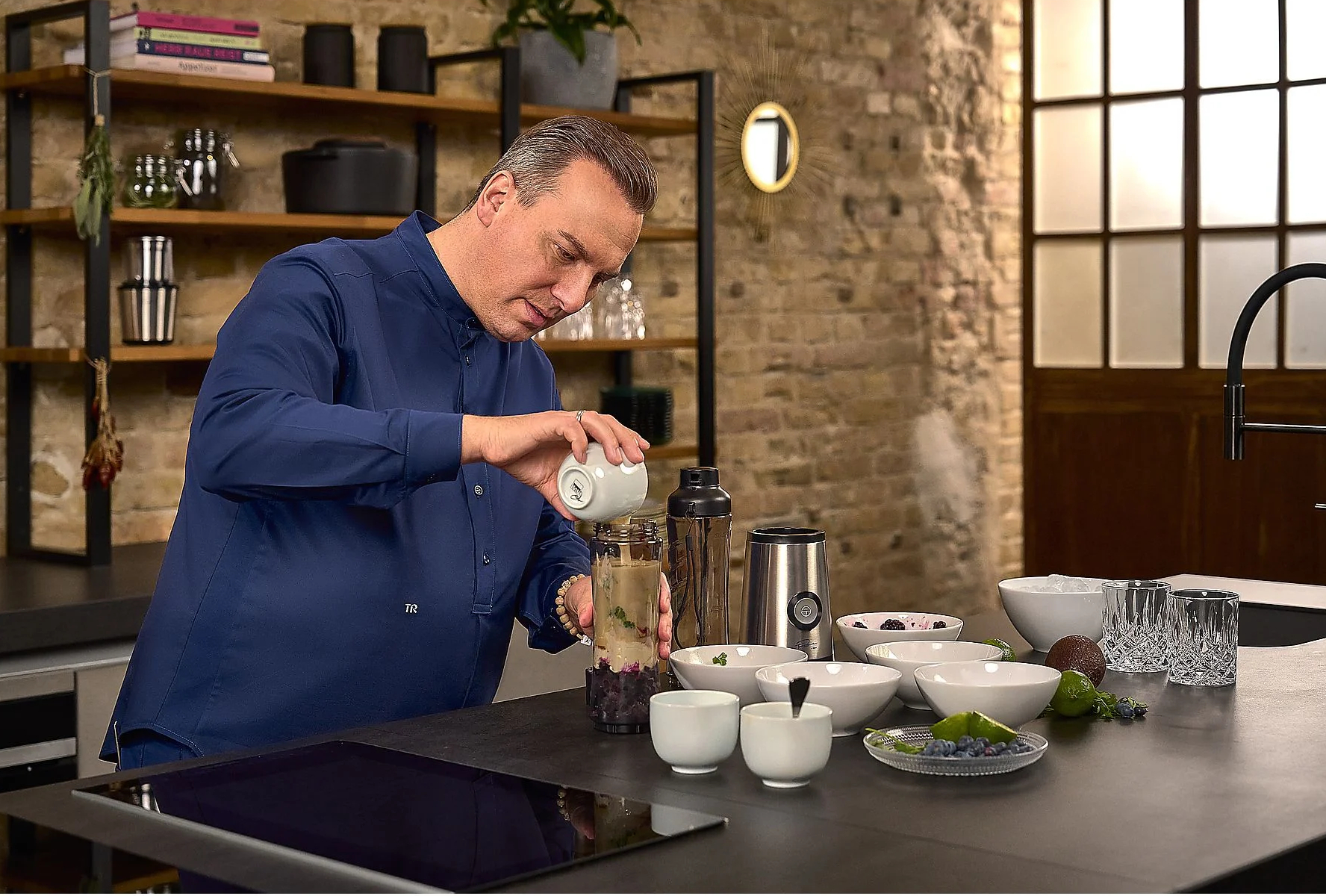 Mężczyzna w niebieskiej koszuli wlewa z małego białego dzbanka do szklanego słoika.